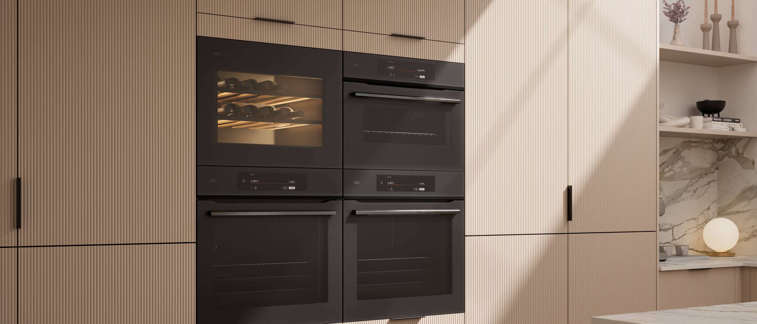 Fluted front kitchen Reed from Magnet in light warm neutral shade Shell, tall cabinets with appliances like ovens and a wine cooler, black handles