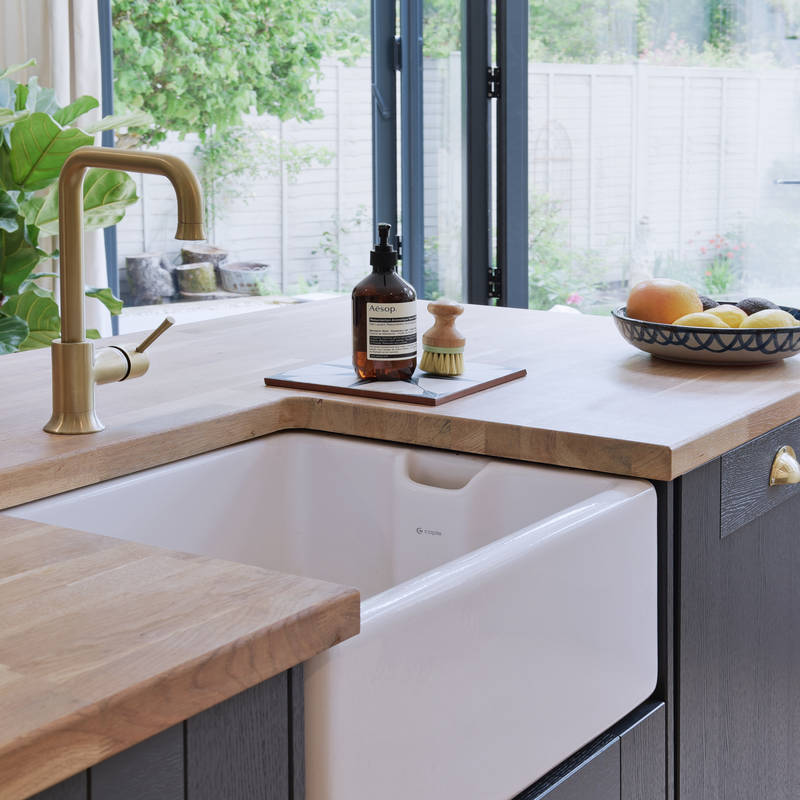 Close-up of Caple Belfast Ceramic sink which adds a rustic charm to the kitchen island. Paired with a wood worktop and brass tap.