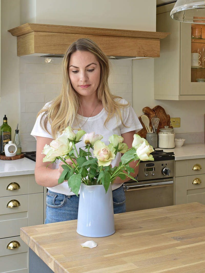Magnet kitchen customer Leanne placing roses in a case on the kitchen island counter in her country cottage.