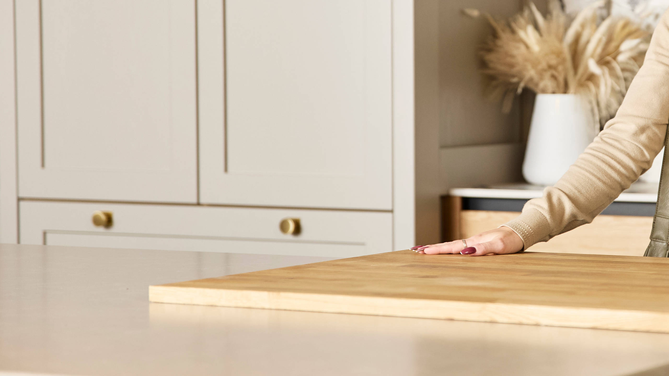 Woman holding a brochure feeling the wood worktop with her hand in a neutral shade Shaker style kitchen in a Magnet Showroom