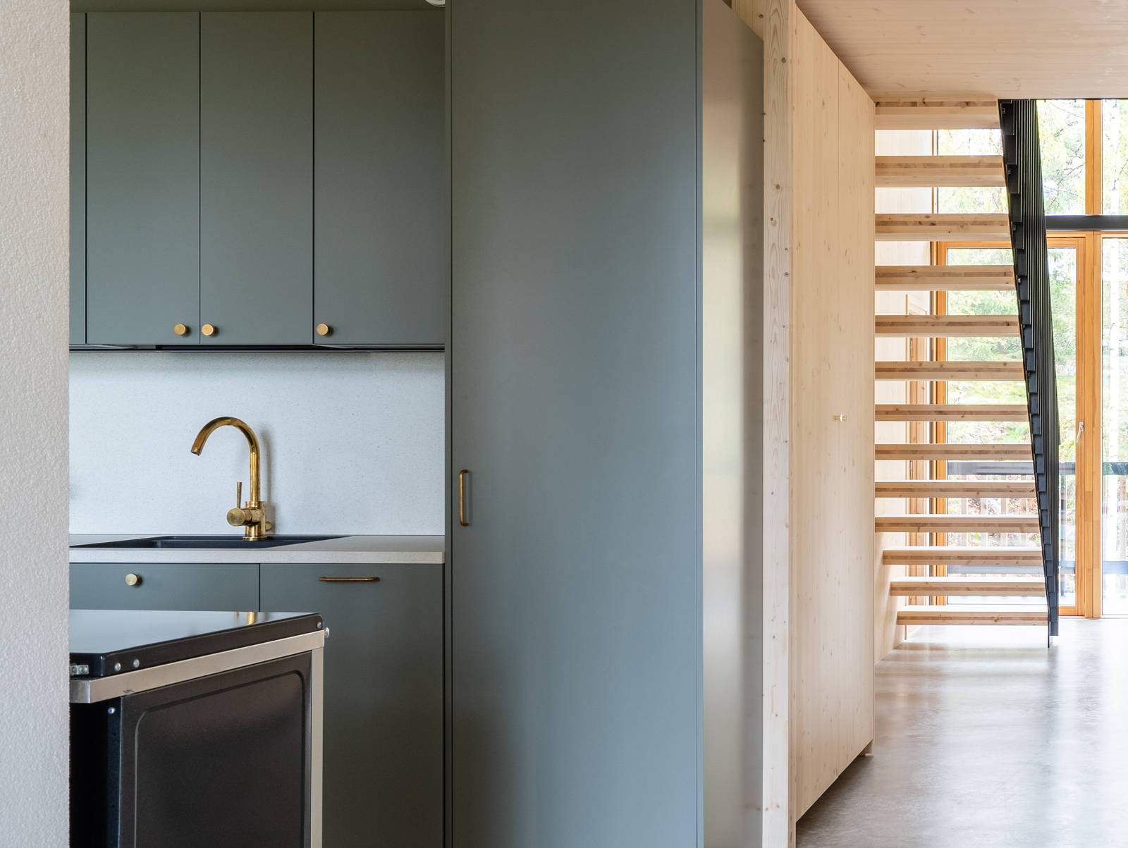 Vihreä keittiö Novartin luonnonvärisessä Havu-sävyssä, messinkinuppeilla, graniittitasoilla ja lasiovilla, joissa on alumiinikehykset keittiön altaassa.