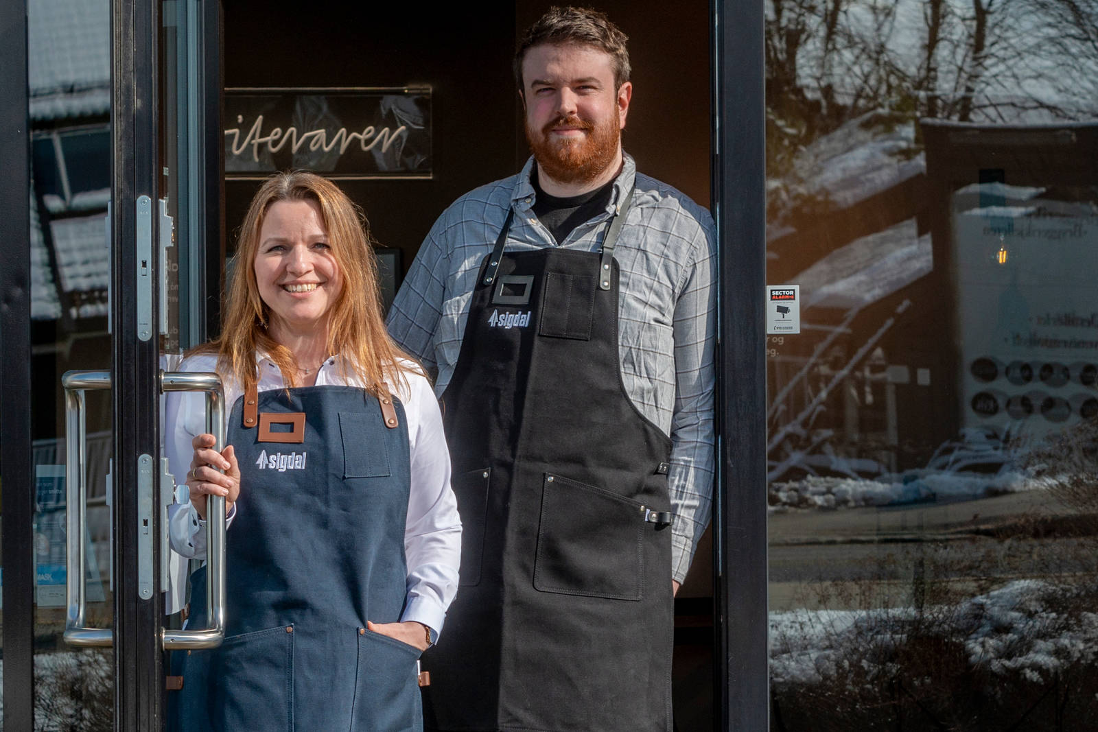 Kjøkkendesignere i skjorter og forklær smiler til kameraet utenfor Sigdals butikk