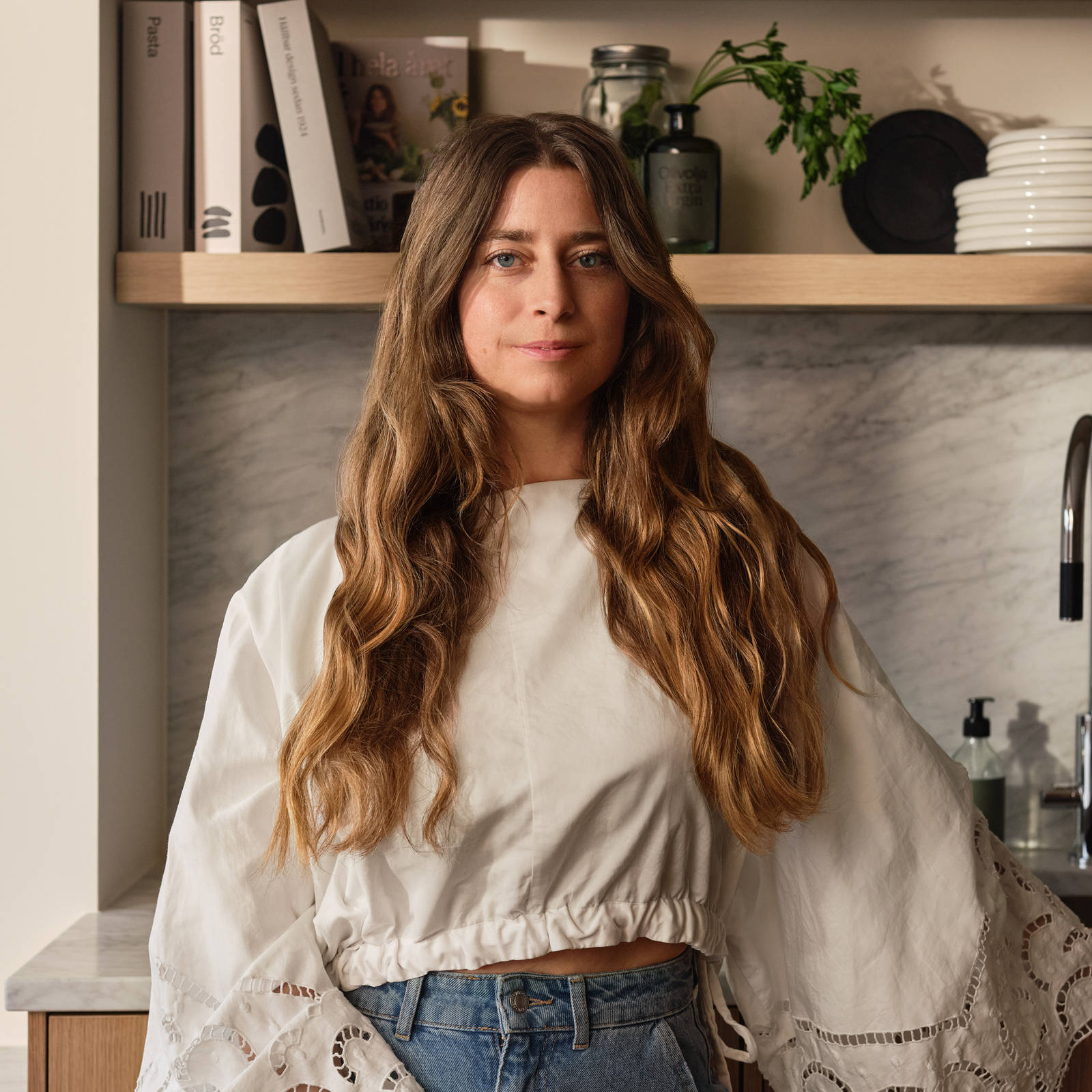 Siri Barje iklädd en ljus stor blus och jeans i sitt kök från Marbodal.