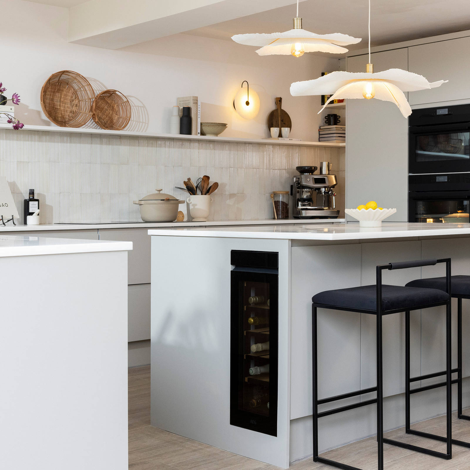 Diagnonal view of kitchen island corner in Yasmin Wyatt's open, light and airy neutral shade handleless Luna kitchen from Magnet with a white Corian worktop in Onyx, two AEG ovens integrated into tall cabinet and a wine cooler integrated into kitchen island.
