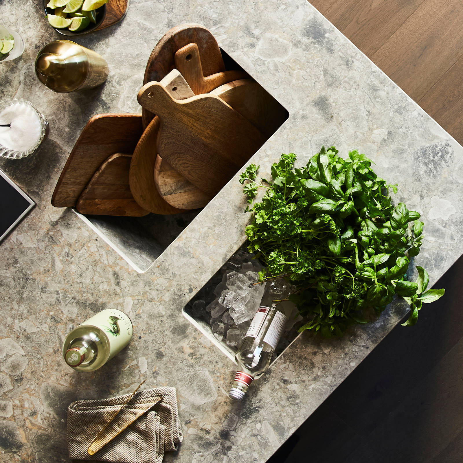 Birds eye view of kitchen island with Dekton in Ceppo worktop,wooden cutting boards with cut up lime fruits and a large plant of basil.