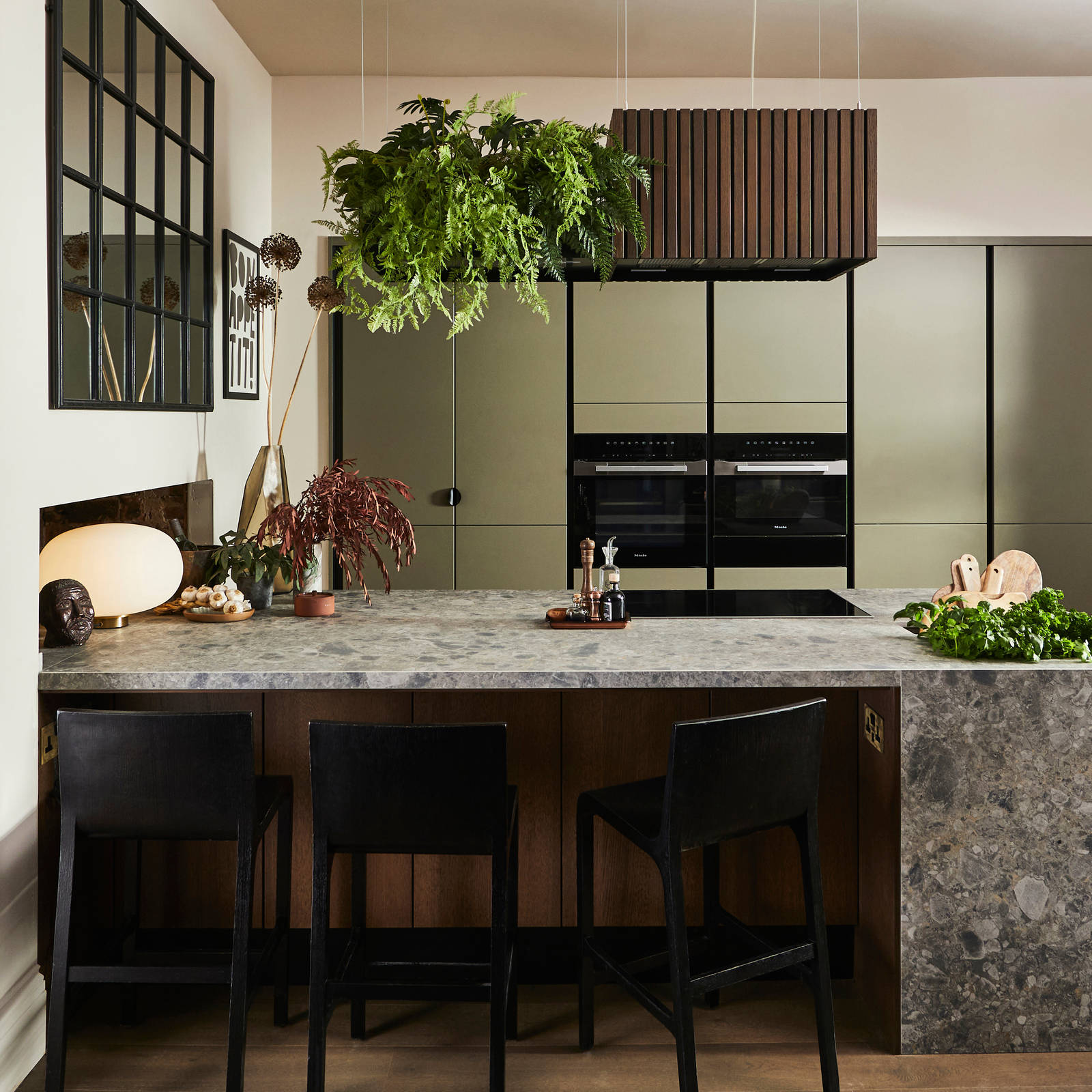 View through opened dark wood doors of the biophilic Dramatic neutral Balmoral Soho and Nordic Nature kitchen from Magnet and matching dark chairs by the bar area of the kitchen island.