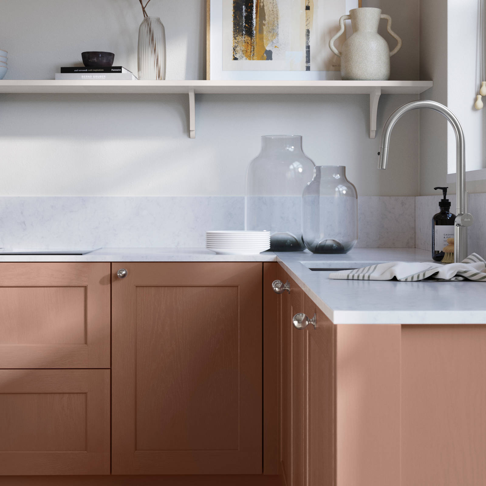 Ludlow, a traditional Shaker-style premium feel kitchen range with a visible woodgrain on its panelled doors here shown in the shade Clay styled with steel knobs, steel tap, a white marbled worktop with matching splashback.
