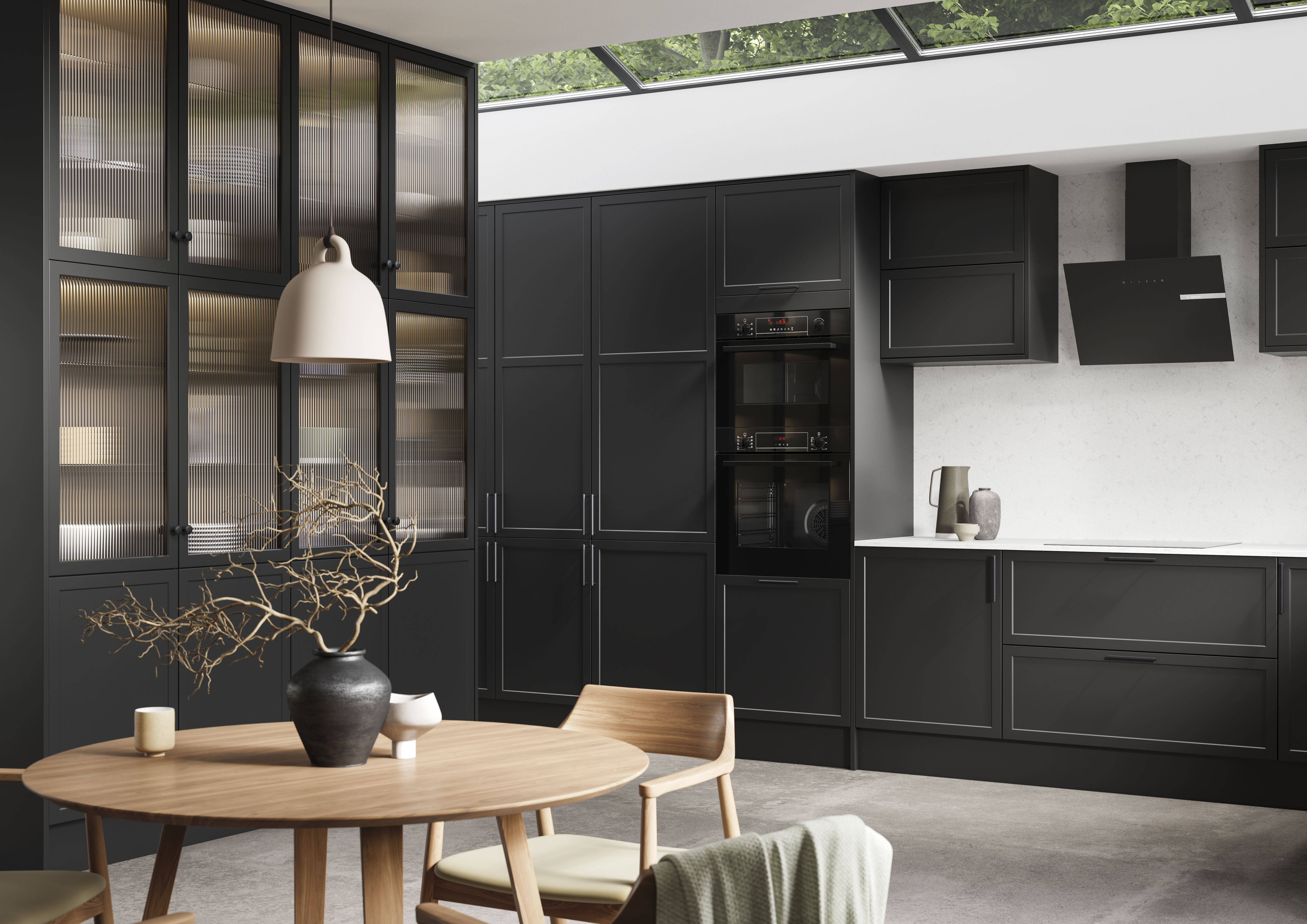 View of modern shaker kitchen Brunswick Sumi Black, with screen extractor over induction hob, tall fluted glass doorsvitrine cabinets, black frame skylights with wood dining table and chairs in foreground.