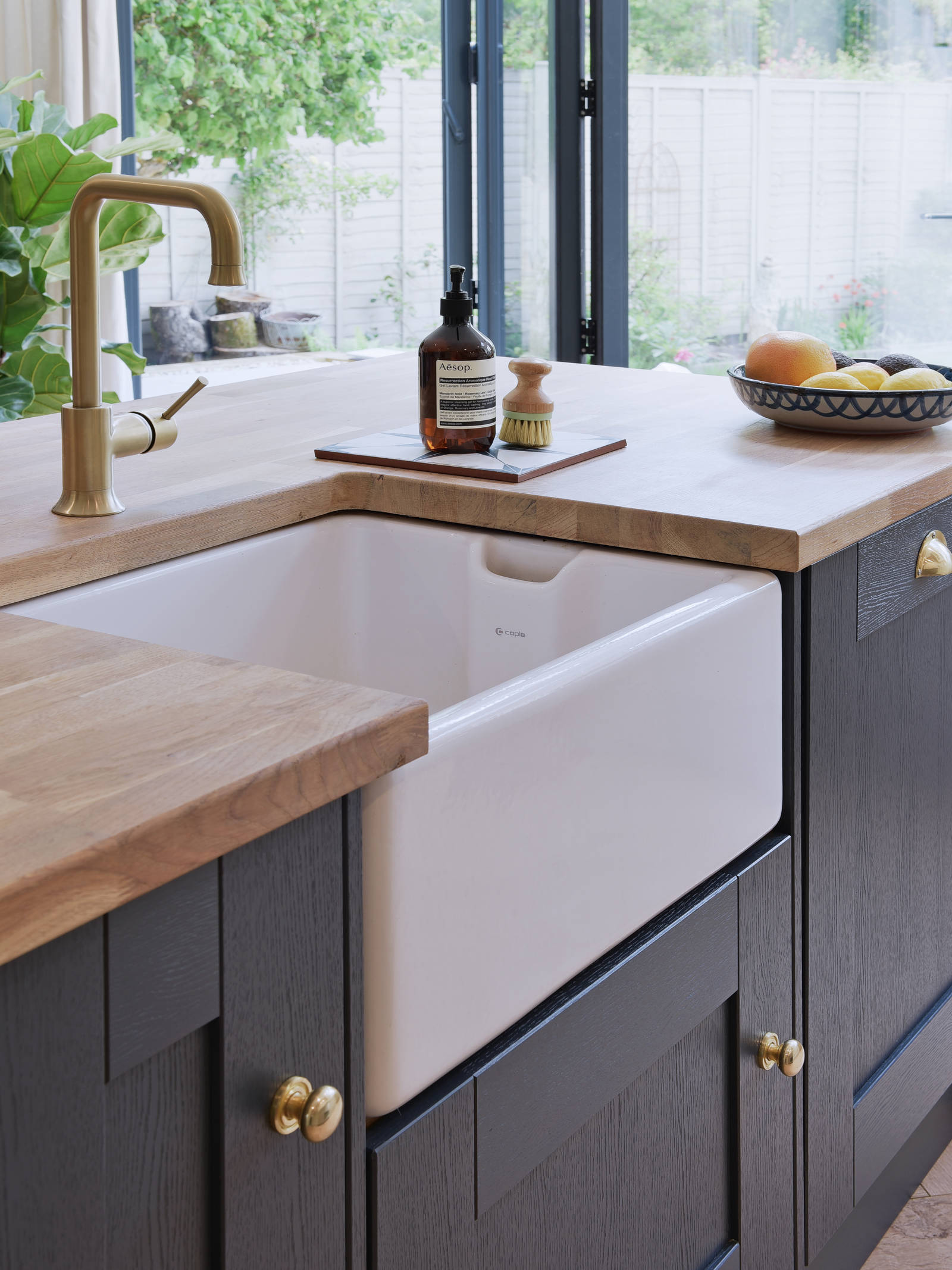 Close-up of Caple Belfast Ceramic sink which adds a rustic charm to the kitchen island. Paired with a wood worktop and brass tap.