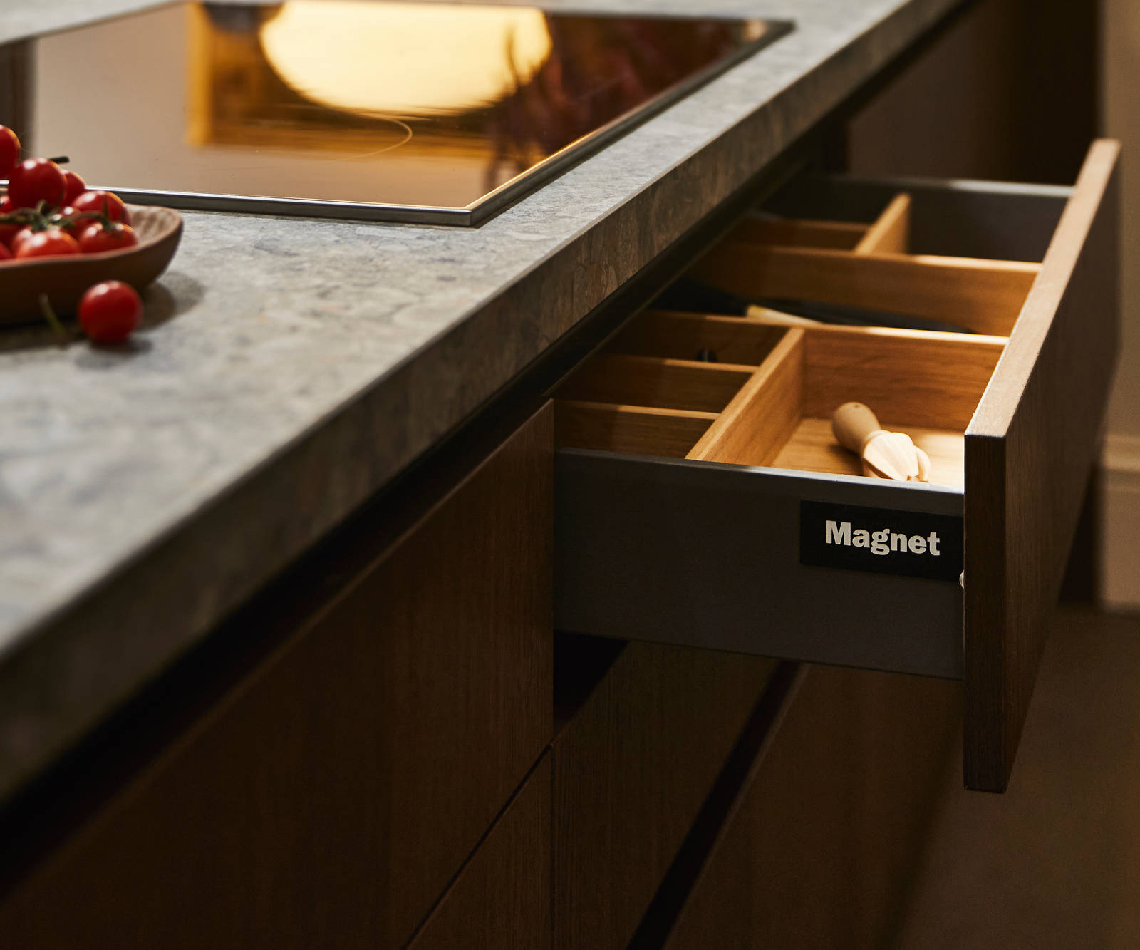 View of kitchen island with an opened Nordic Nature drawer containing oak inserts, a Dekton in Ceppo worktop and potted plants in background.