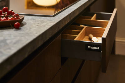 View of kitchen island with an opened Nordic Nature drawer containing oak inserts, a Dekton in Ceppo worktop and potted plants in background.