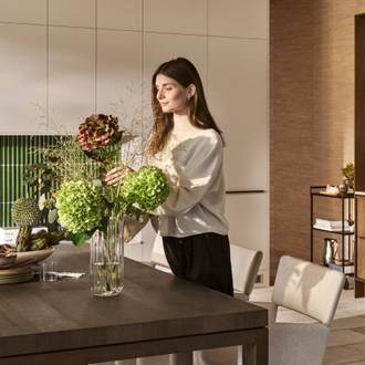 Kvinde sætter blomster i vase i mørk eg Forever Oak køkken fra INVITA i køkkenet med overskabe og højskabe i Athena Sand