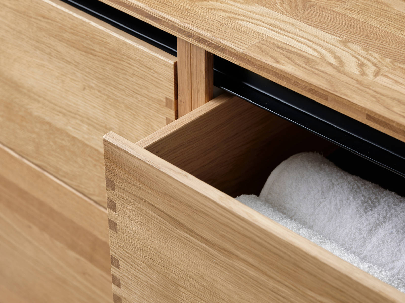 Nærbillede av åben badeværelsesskuffe i massiv egetræ badeværelsesmøbel GLØD fra INVITA med fingertappede samlinger og grebsløse skuffer
