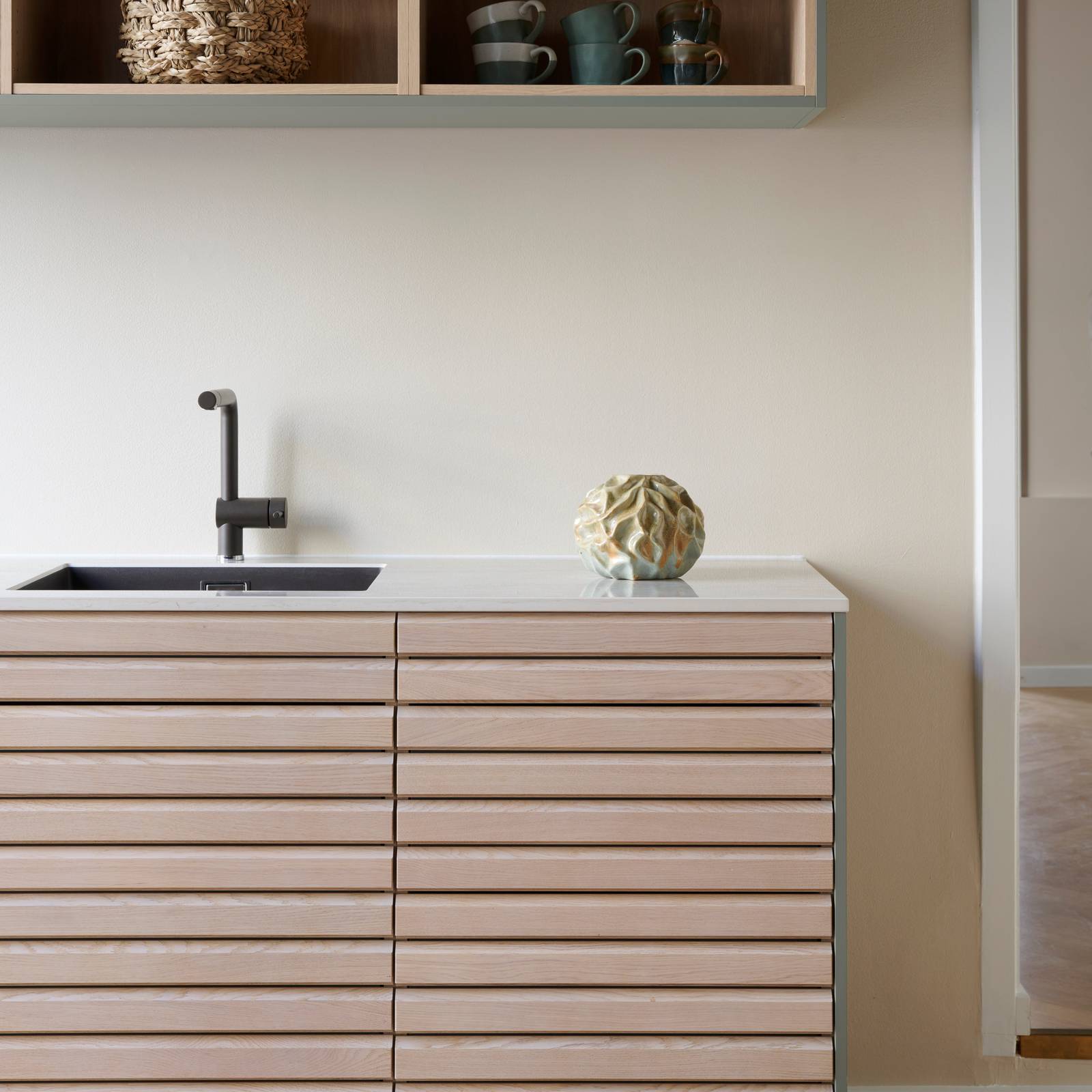 Nærbillede af egetræskøkken Ikon med håndsorterede lameller i massiv eg, kombineret med overskabe og åbne væghylder grebsfrie grønne køkkenet Highline Salvie med indfræsede greb i lågerne fra INVITA