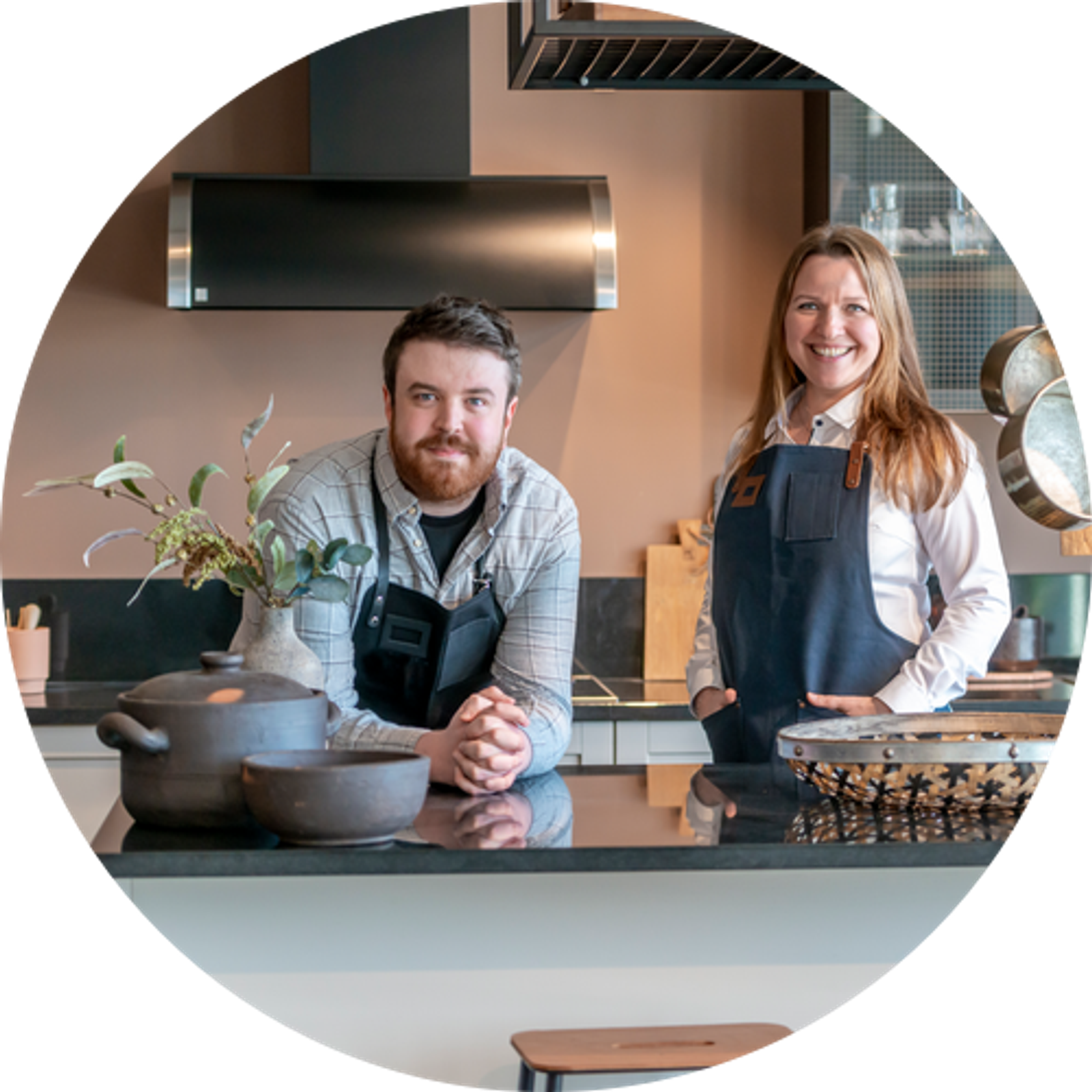 Kjøkkendesignere iført skjorter og blå forklær smiler til kameraet utenfor Sigdals butikk