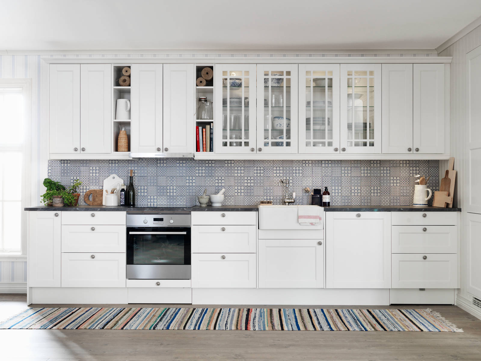 Marbodal Fagerö Frost - kök med vitrin, matchande kakel och lugna färger med en känsla av skärgård och med en flirt åt tidigt 1900-tal. Bänkskivan med stenkaraktär och en tidstypisk blandare i nedfälld porslinsho förstärker intrycket.