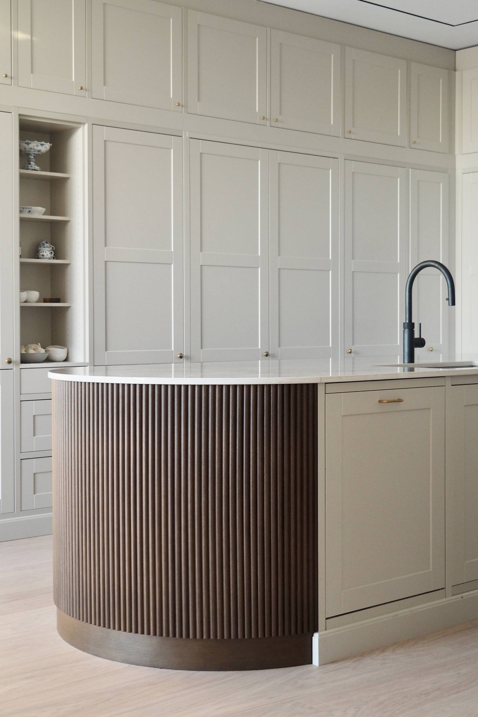 Enden af ​​den afrundede køkkenø med mørkt træpanel, Dekton Taga bordplade og sorte barstole