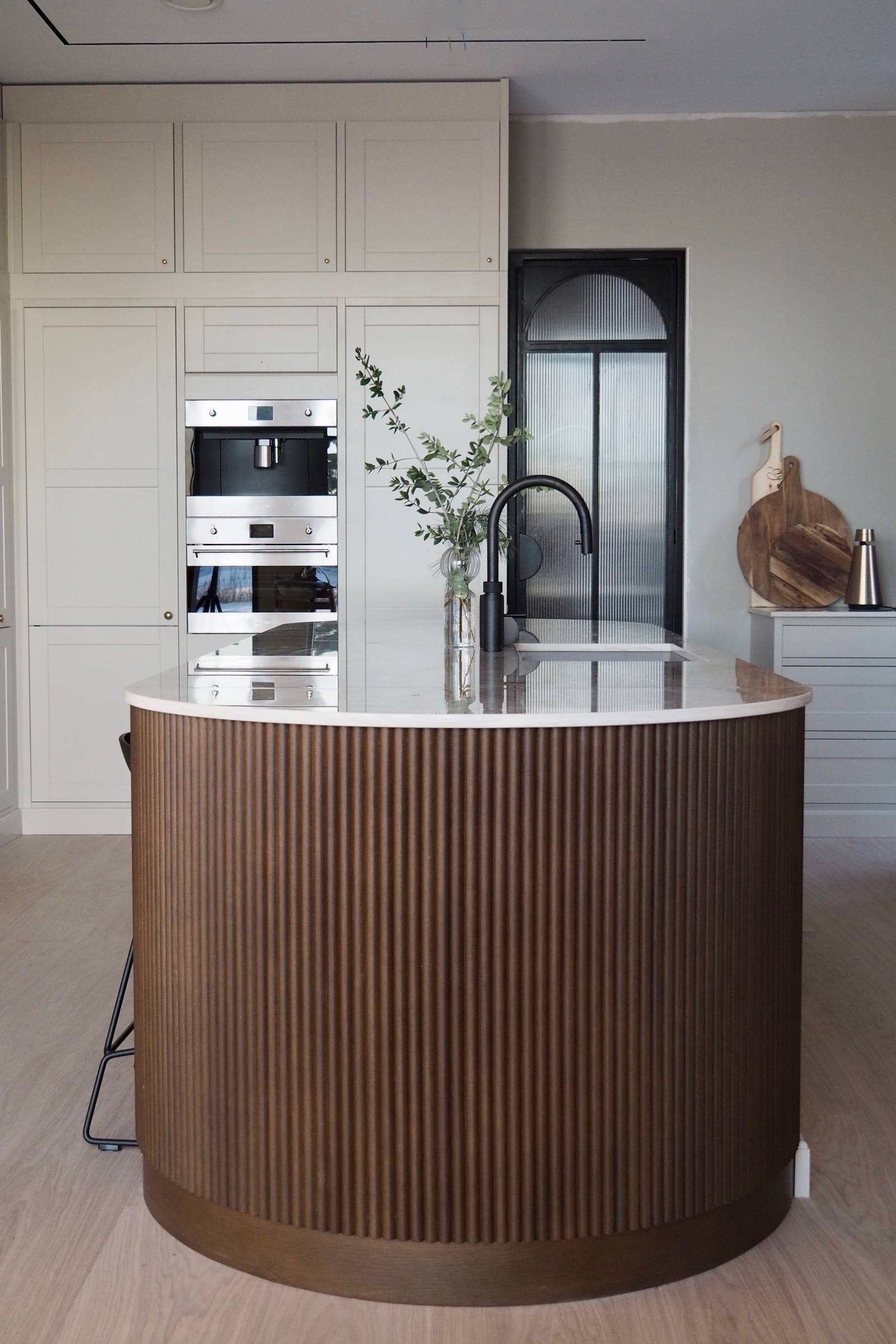 Enden af ​​den afrundede køkkenø med mørkt træpanel, Dekton Taga bordplade og sorte barstole