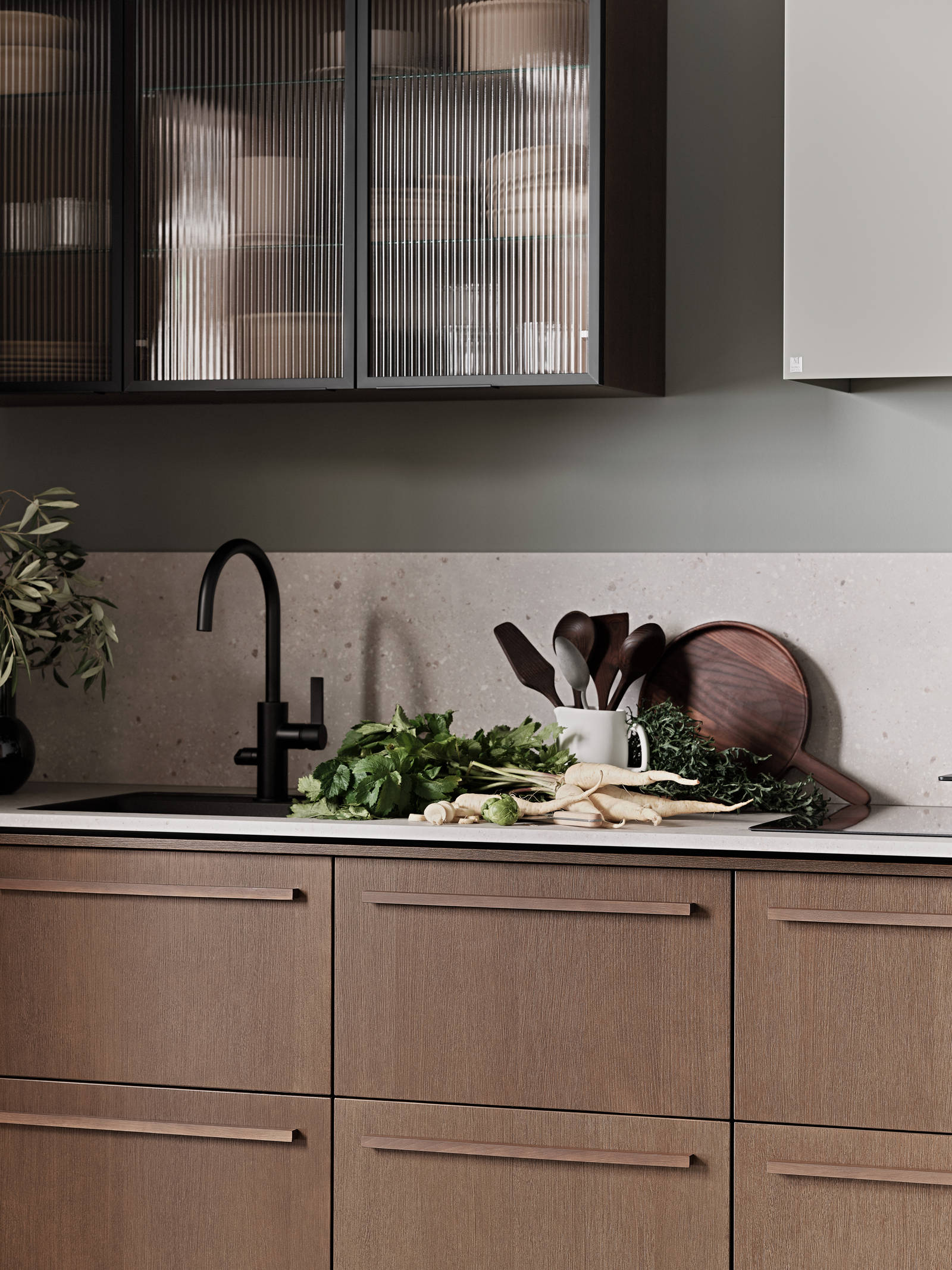 Nærbillede af Køkken Forever Oak fra INVITA, mørk eg køkkenskabe med massiv tre mørk eg håndtag, komposit bordplade, sort armatur og vitrineskab med riflede glas i tynd, sort aluminiumsramme