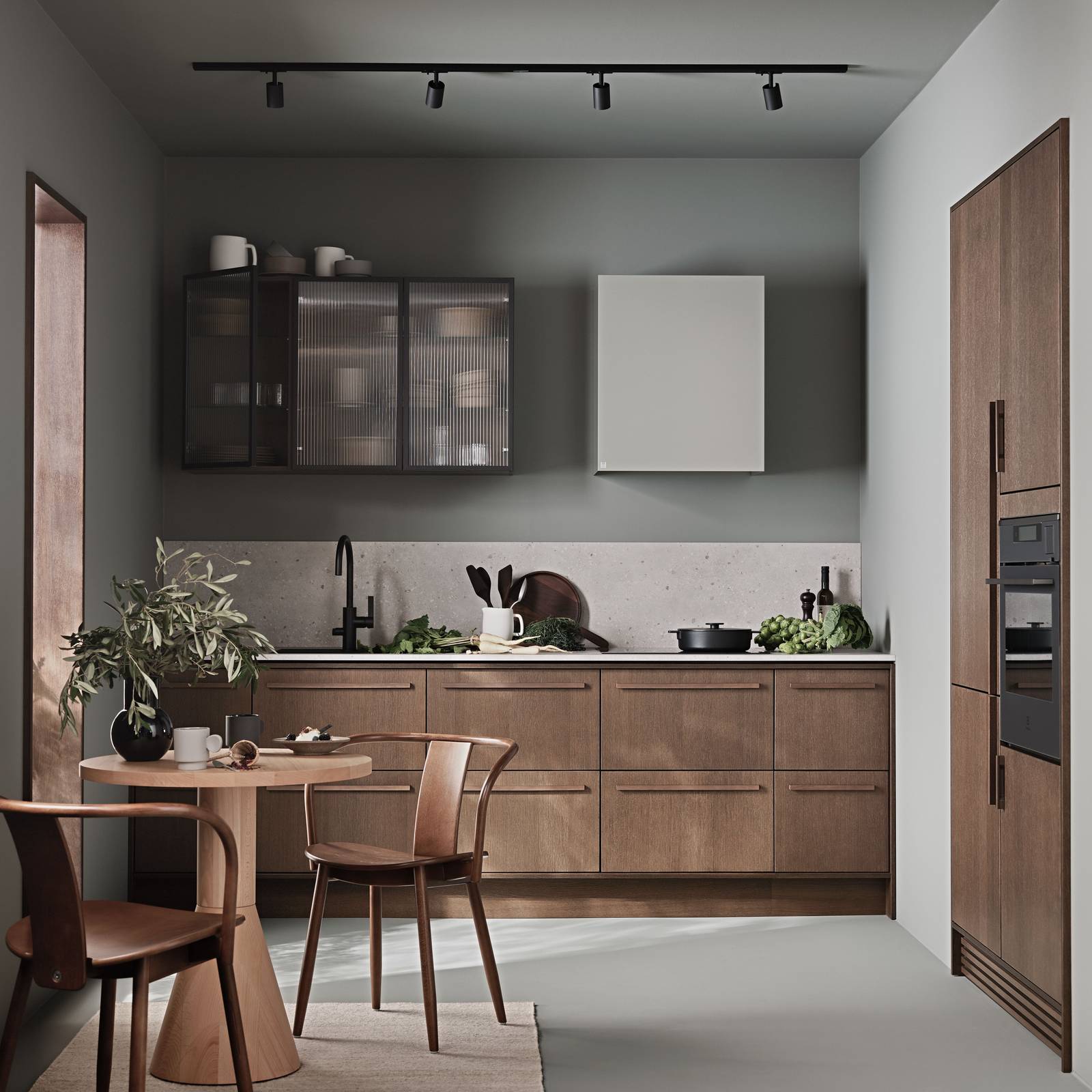 Køkken Forever Oak fra INVITA, mørk eg køkkenskabe med massiv tre mørk eg håndtag, komposit bordplade, sort armatur og vitrineskab med riflede glas i tynd, sort aluminiumsramme