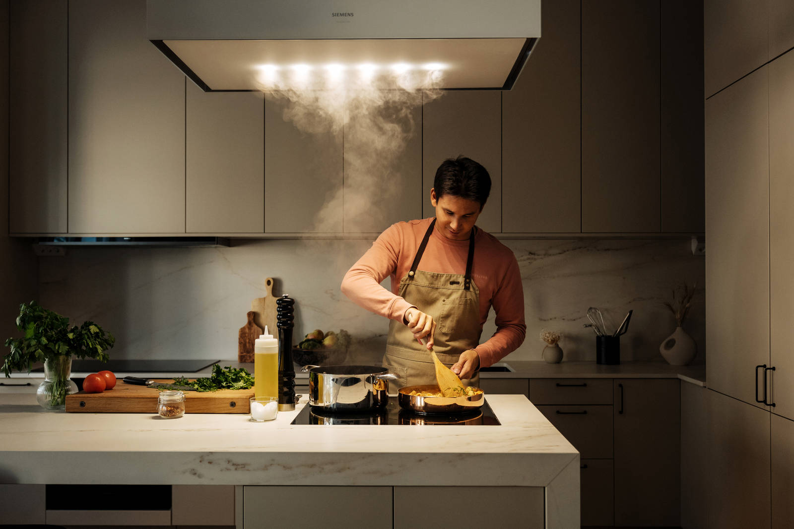 Filip Poon lagar mat i sitt clean och eleganta Arkitekt Plus Sand-kök från Marbodal med Dekton-bänkskiva och matchande stänkskydd