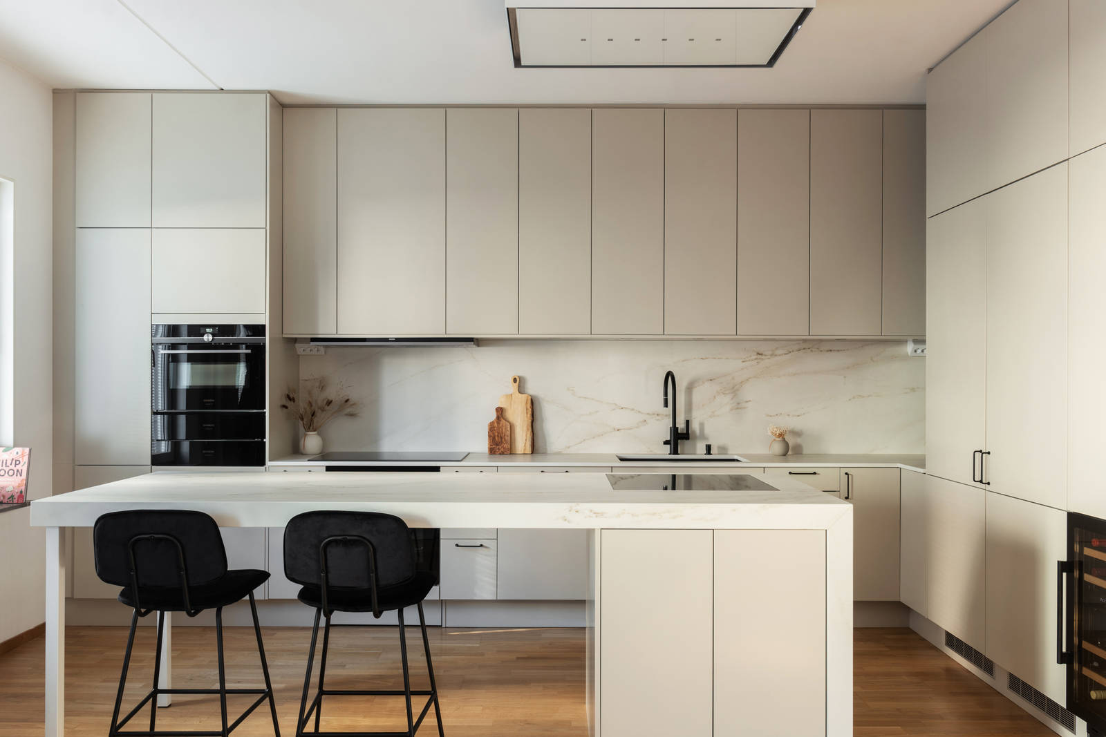 Köksö med två spishälar och barstolar i Filip Poons kök från Marbodal, Arkitekt Plus Sand med svarta handtag och Dekton bänkskiva samt stänkskydd