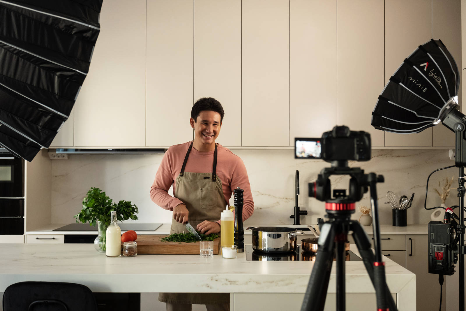 Filip Poon lagar mat framför kameran i sitt clean och eleganta Arkitekt Plus Sand-kök från Marbodal med Dekton-bänkskiva och matchande stänkskydd