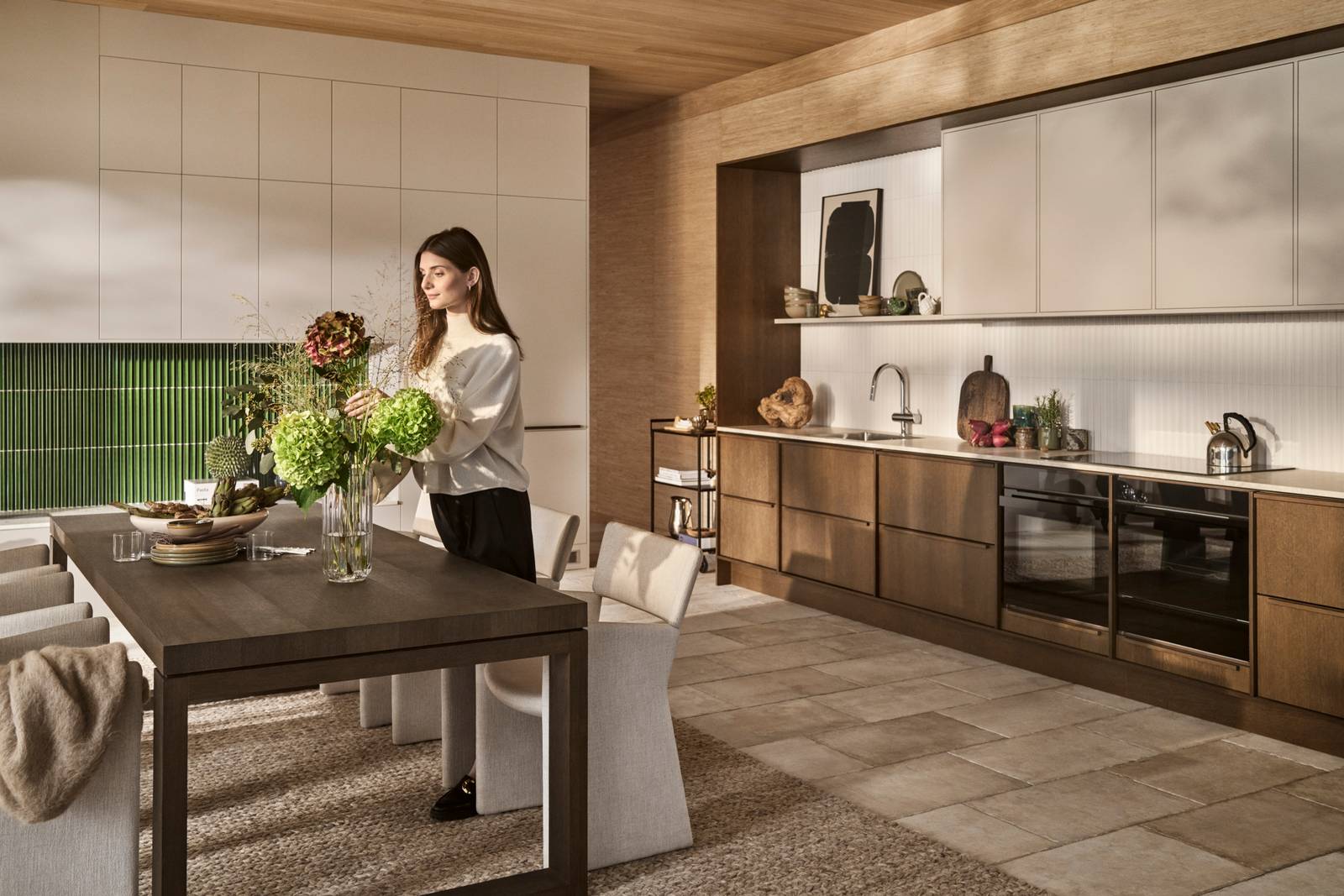 Kvinde sætter blomster i vase i mørk eg Forever Oak køkken fra INVITA i køkkenet med overskabe og højskabe i Athena Sand