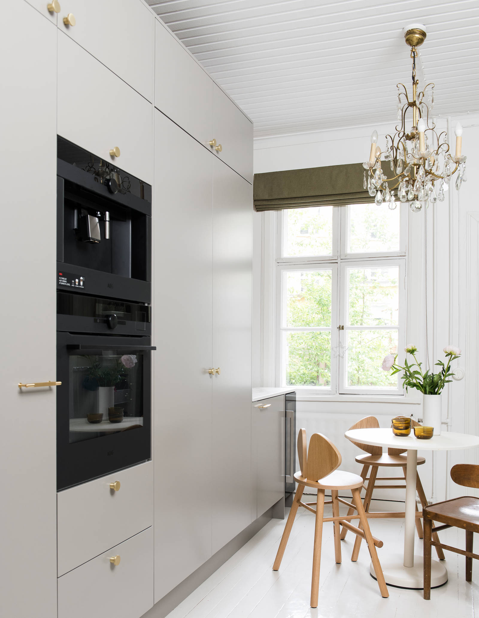 Tähkä Taupe sileämaalattu keittiö messinkinupeilla, sisäänrakennettu uuni ja kahvinkeitin korkeissa kaapeissa, pöytä puutuoleineen