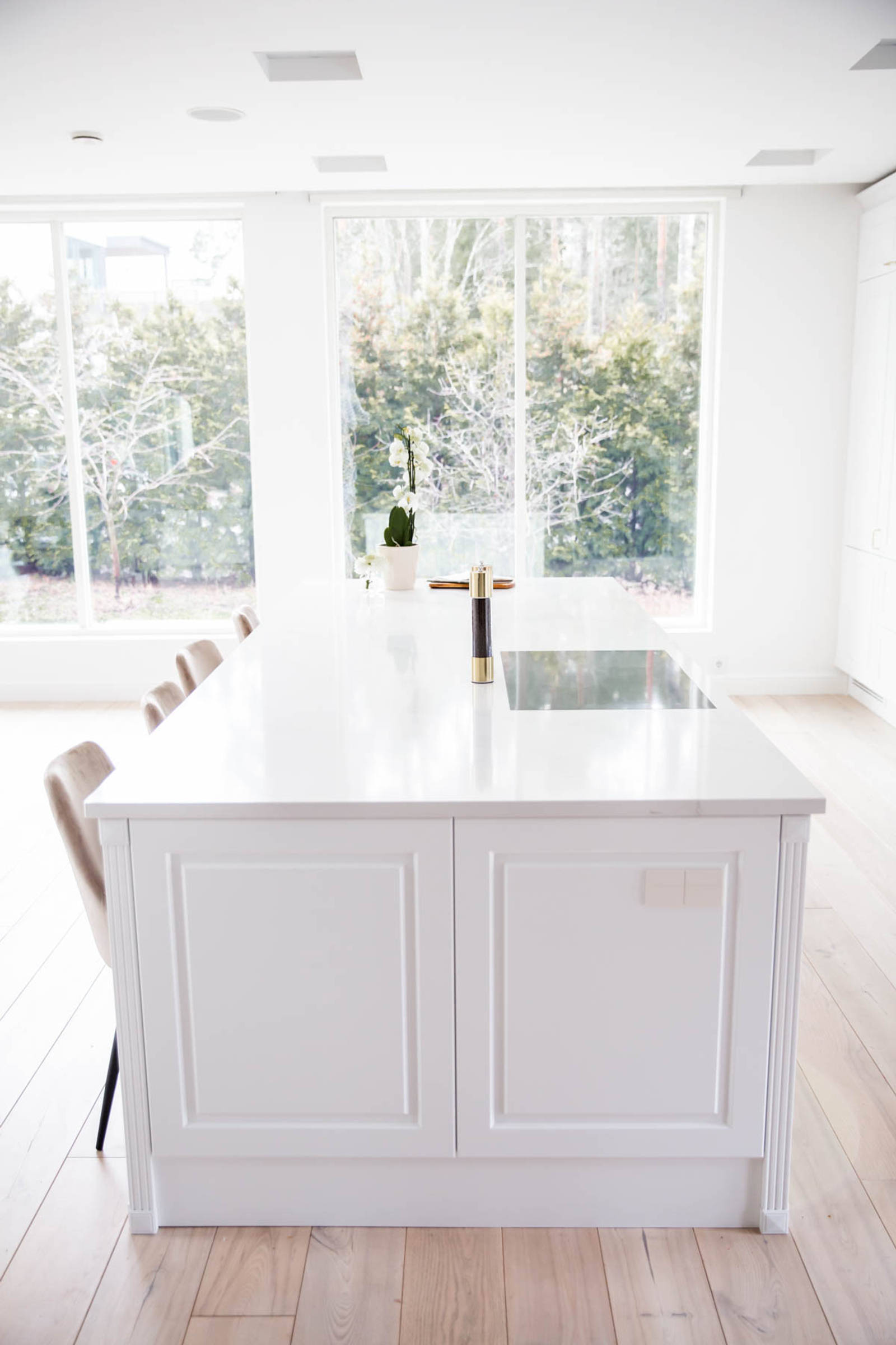 Valkoinen keittiö, jossa perinteiset maalatut karmiovet, messinkikahvat ja marmoroitu työtaso, keittiösaareke istuimilla.