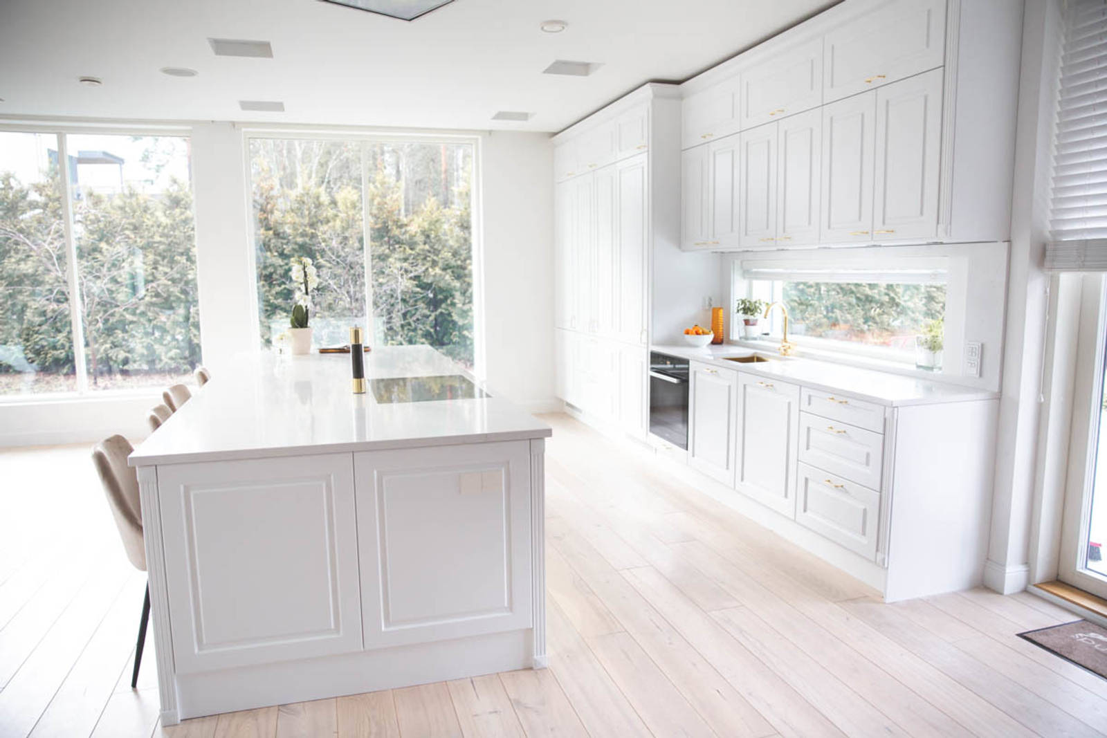 Valkoinen keittiö, jossa perinteiset maalatut karmiovet, messinkikahvat ja marmoroitu työtaso, keittiösaareke istuimilla.