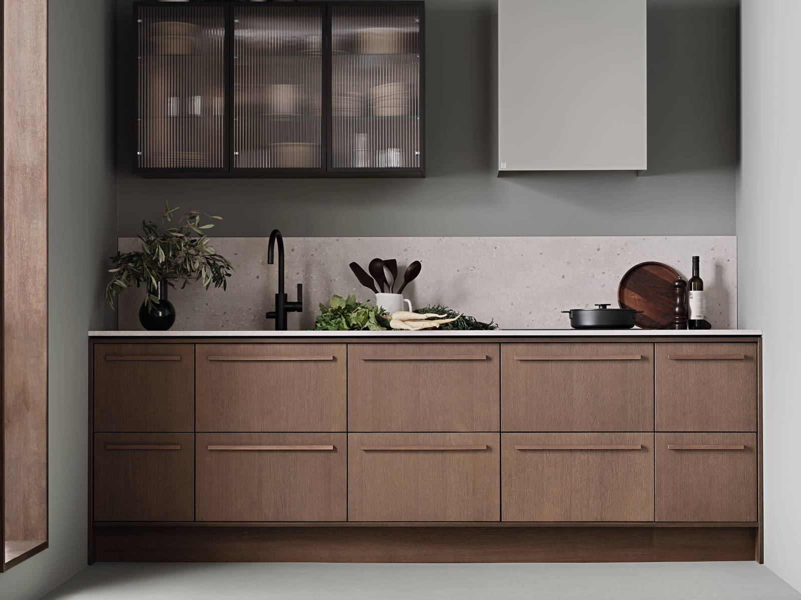 Køkken Forever Oak fra INVITA, mørk eg køkkenskabe med massiv tre mørk eg håndtag, komposit bordplade, sort armatur og vitrineskab med riflede glas i tynd, sort aluminiumsramme