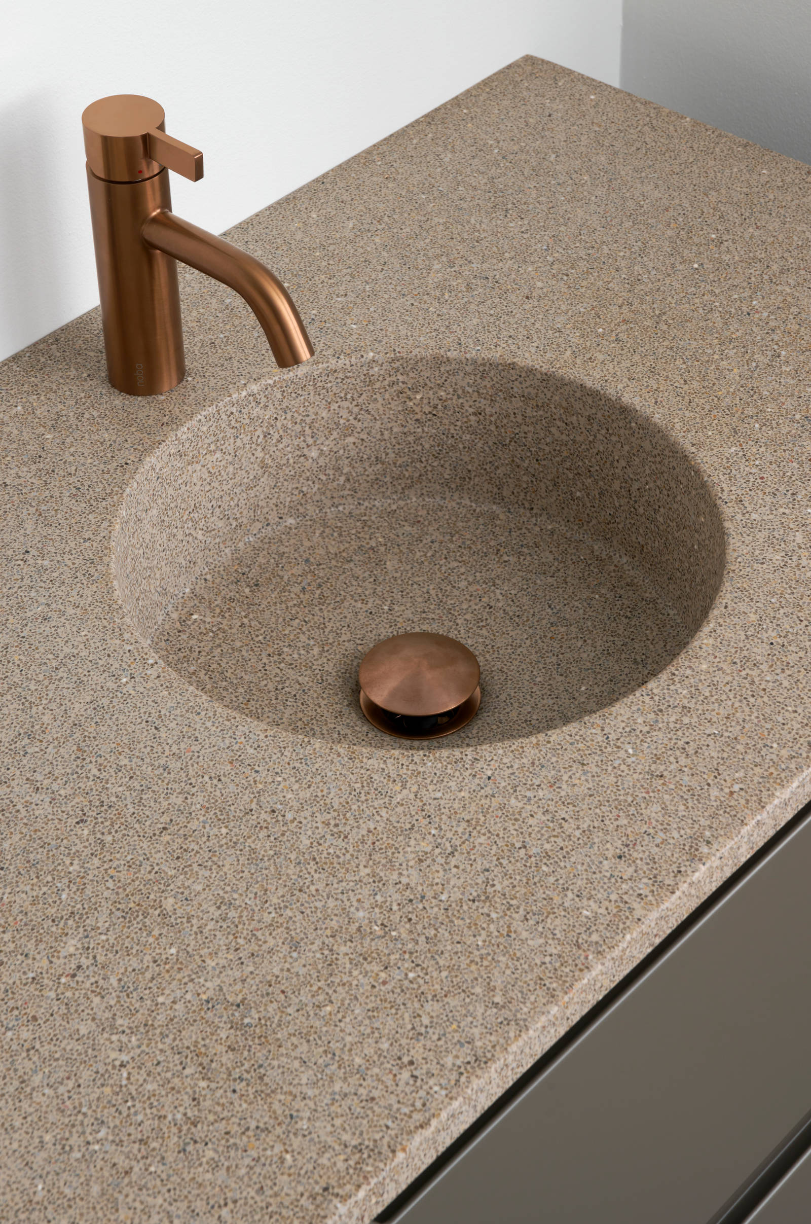 Nærbillede af bordplade stone beige 99 med vask cannes-30-30 og Cassøe borstet kobber armatur i moderne badeværelsesmøbel Urban med indfræsede greb i brune farve Bark og