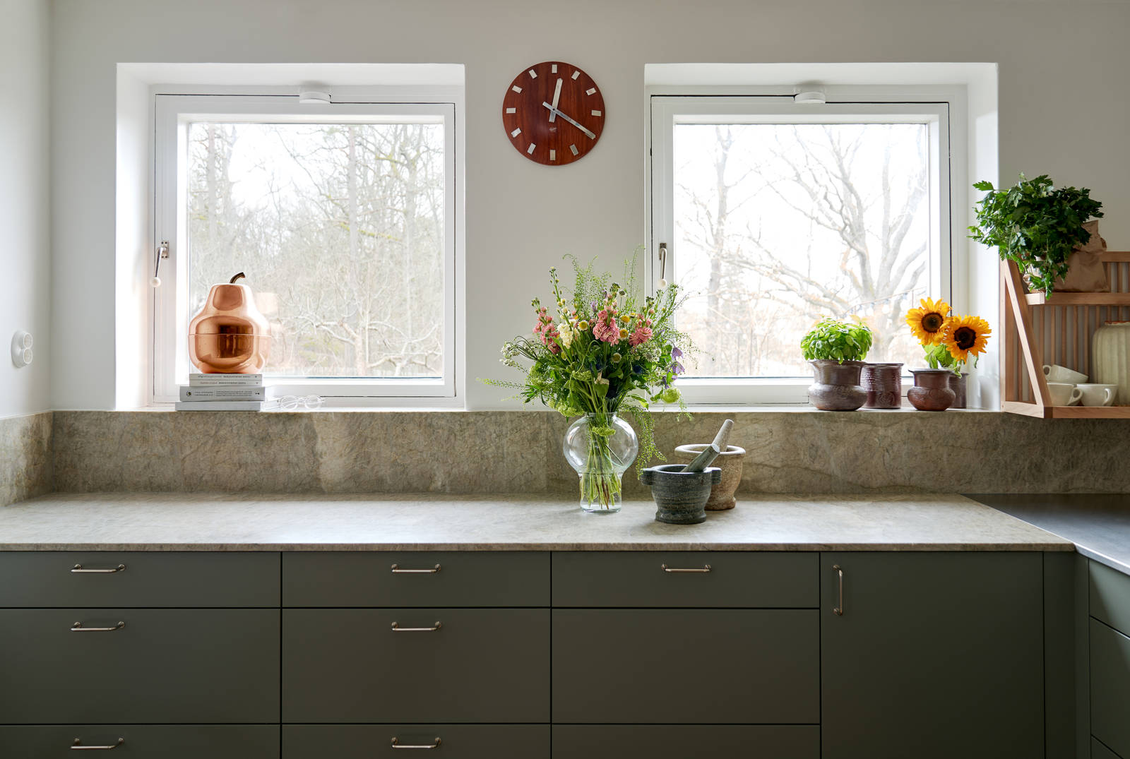 Inredningsprofilen Svante Öquists kök från Marbodal, Arkitekt Plus i den gröna kulören Tall med bänkskiva och matchande stänkskydd i kvartsit. Två stora mortar i marmor vilar på bänkskivan.