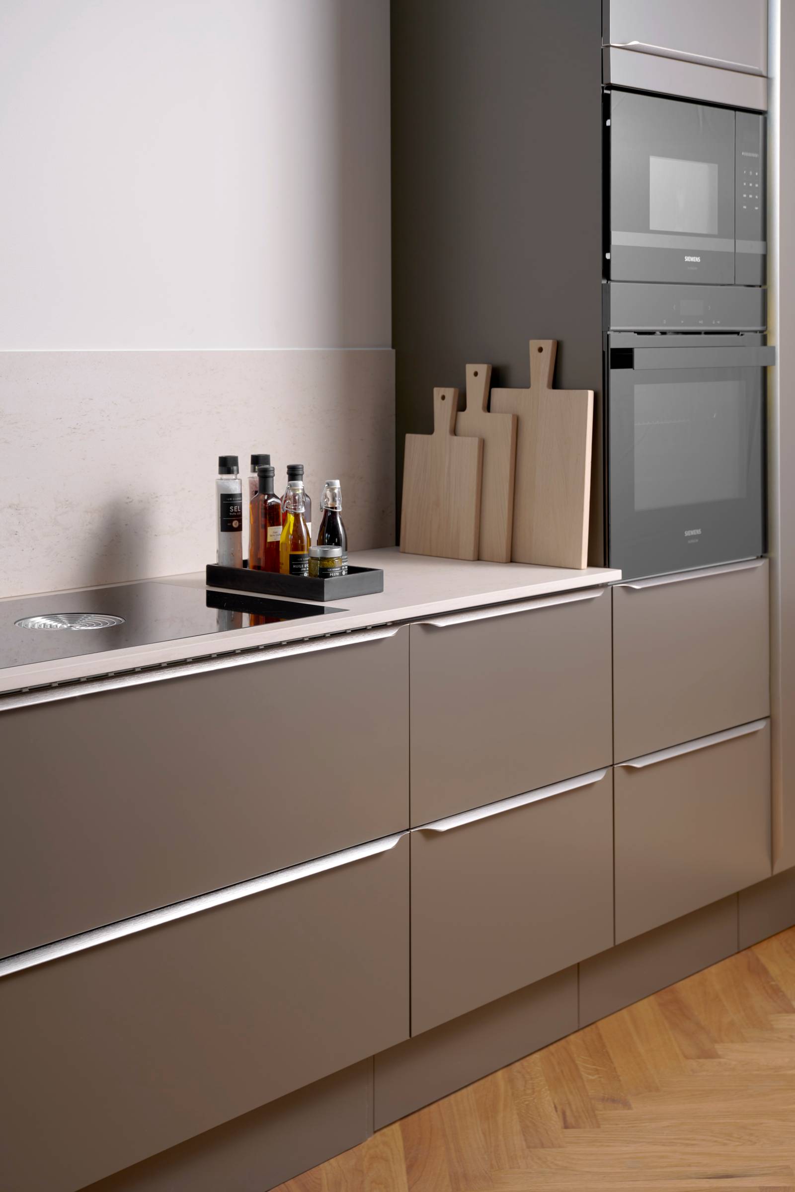 Minimalistisk brun køkken Newline Bark fra INVITA med indbygningsovne i højskabe, diskret greb i stål og lys beige bordplade med matchende splashback