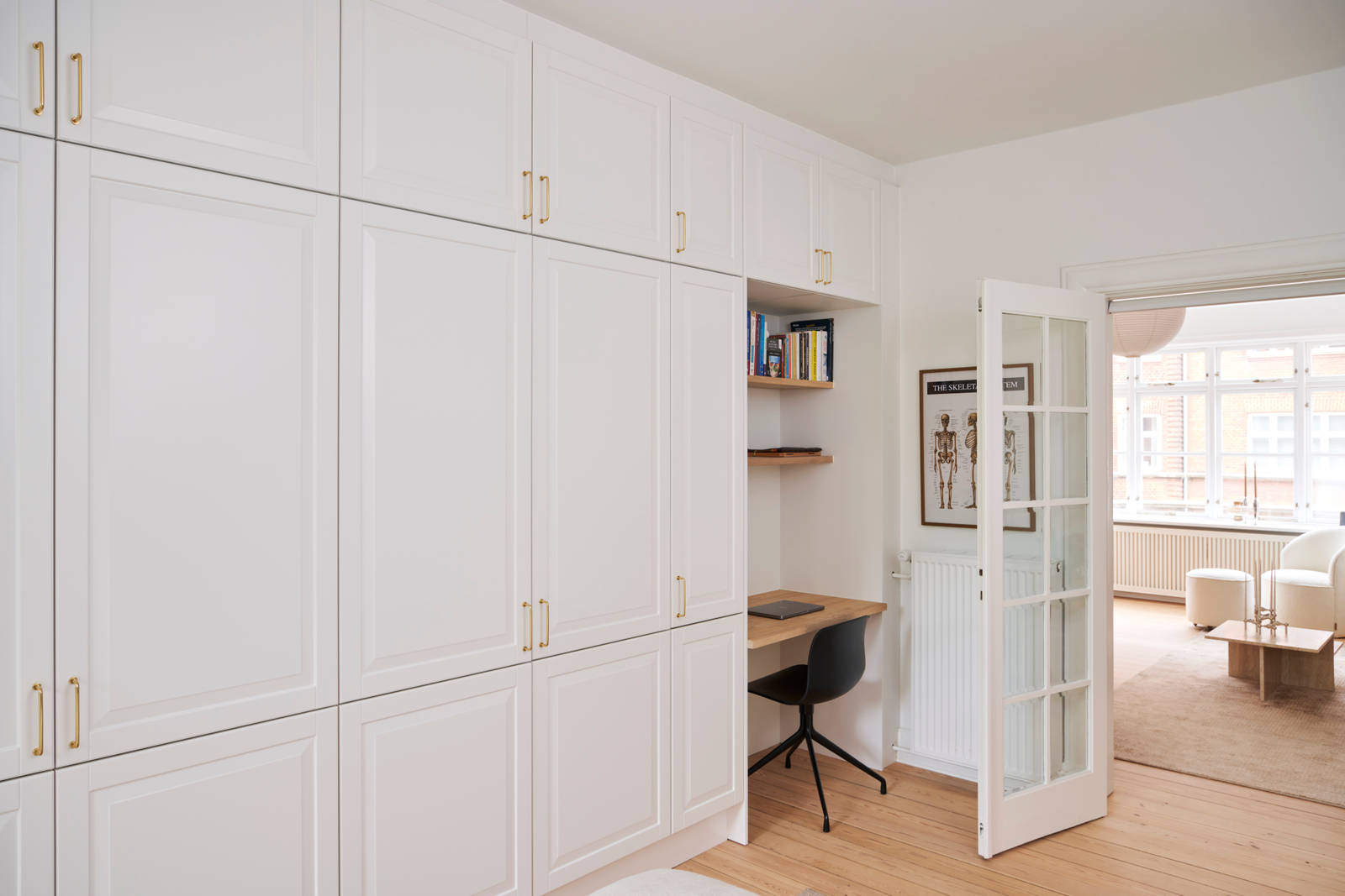 Hvid garderobe Nordic Frost fra INVITA med fyldningslåger og messinggreb, med indbygget bordplade med stol og væghylder til hjemmekontoret