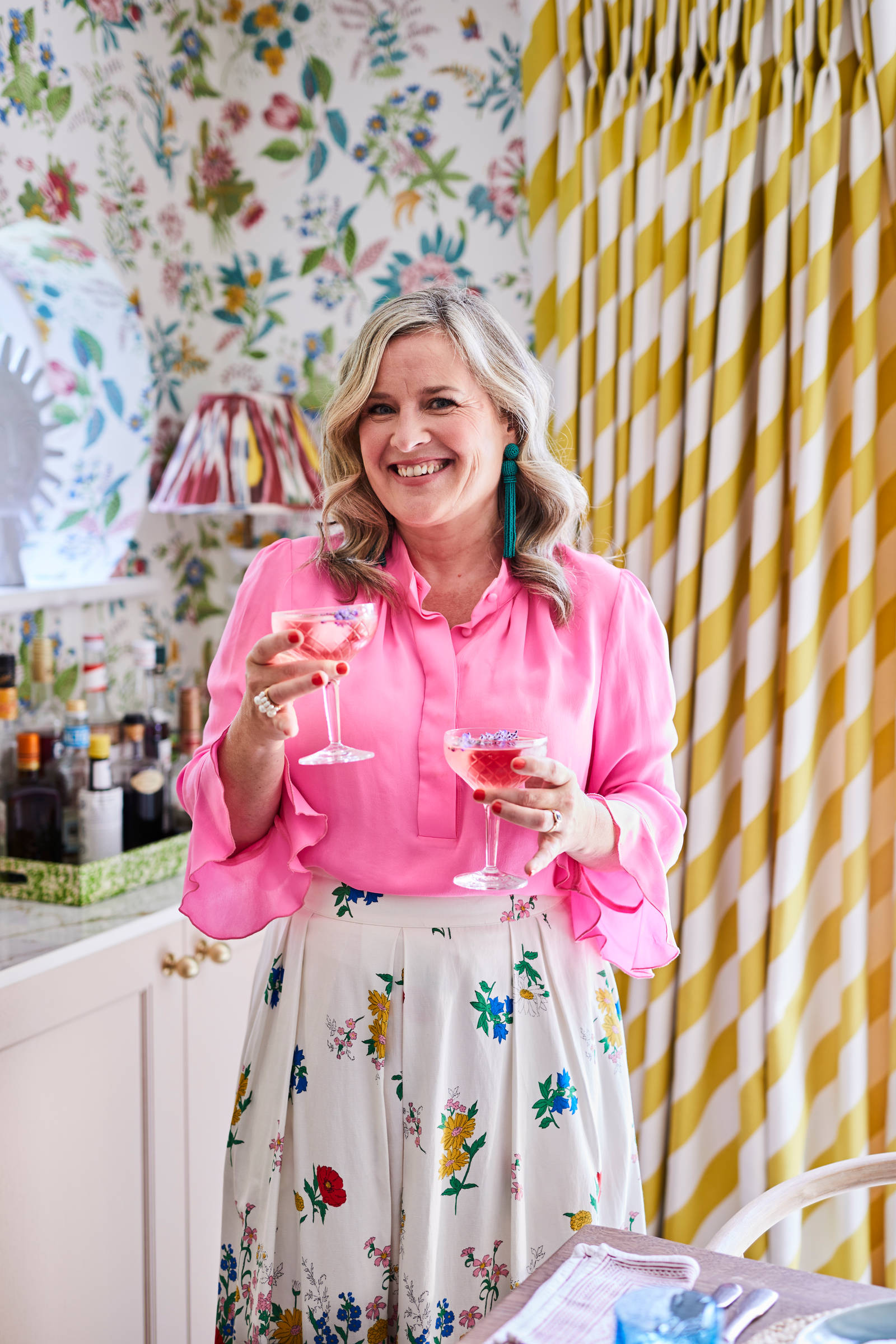 Sophie smiling and wearing vibrant colors, holding two drinks in the Cocktail corner