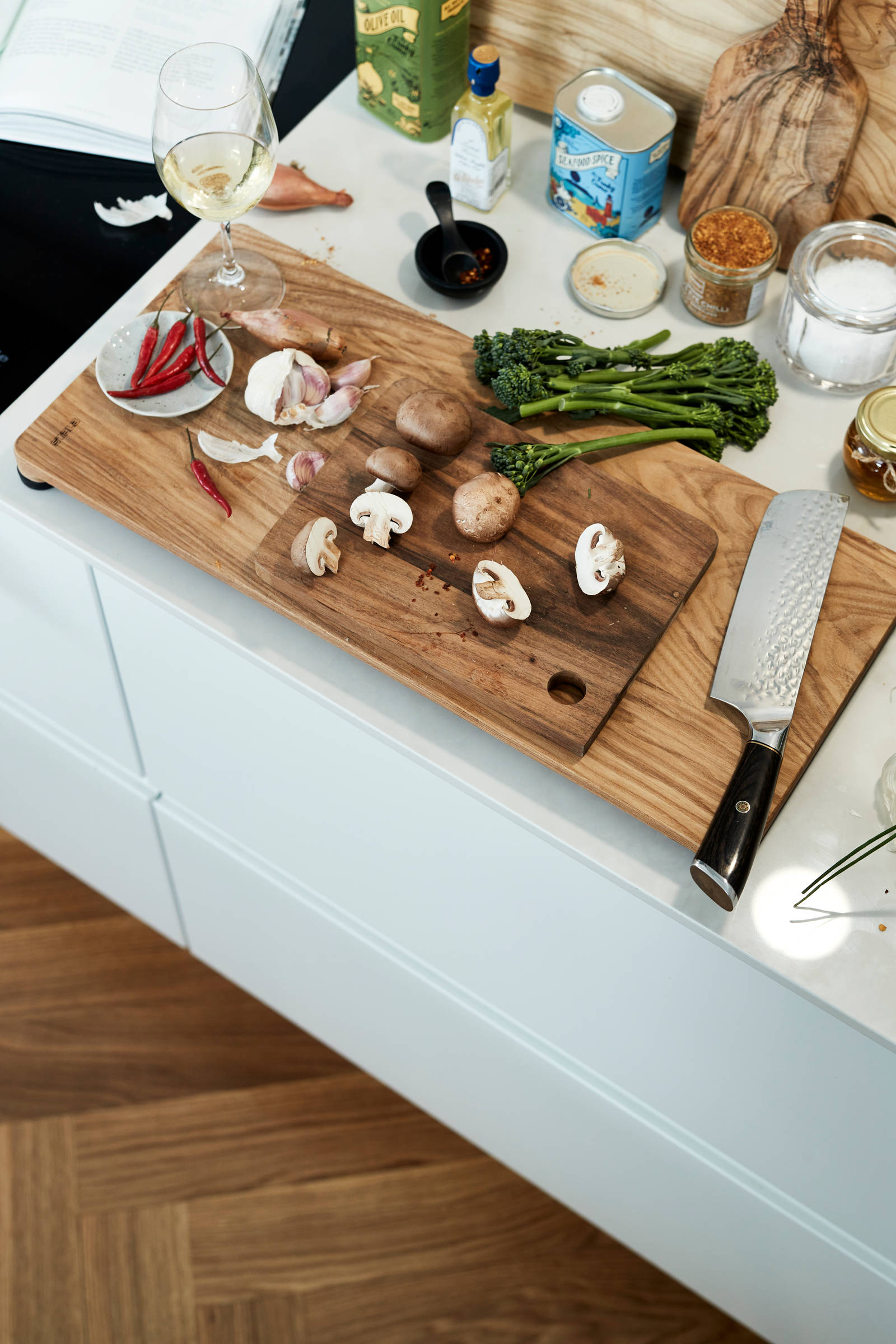 Vihanneksia ja sieniä puisella leikkuulaudalla työtasolla, Valkoinen keittiö, jossa sisäänrakennettu kahvaura ovessa, Dekton Helena kivitaso ja siihen sopiva roiskepala