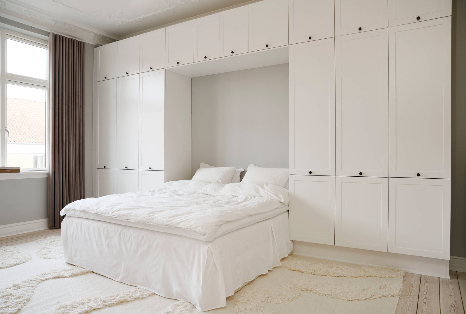 Hvid tidløs garderobe Square Sand fra INVITA omkring en seng med en kommode over, sorte greb på karmdøren