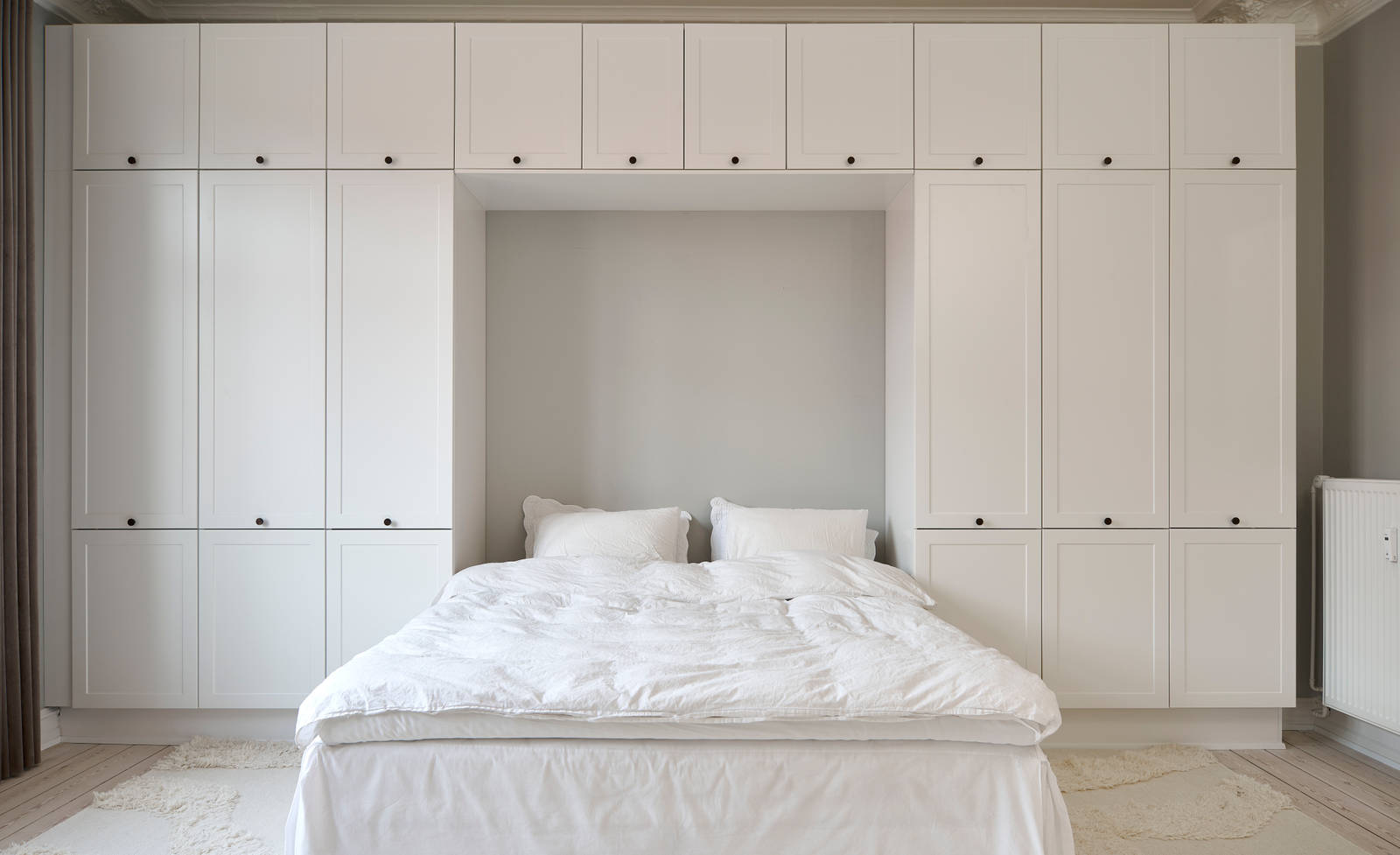 Hvid tidløs garderobe Square Sand fra INVITA omkring en seng med en kommode over, sorte greb på karmdøren