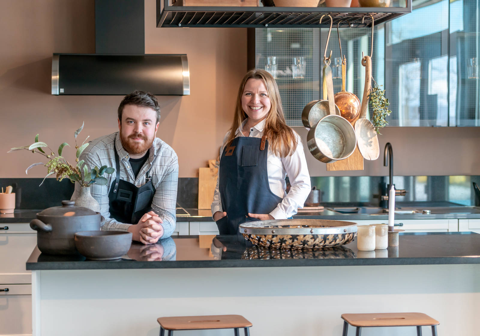 Kjøkkendesignere iført skjorter og blå forklær smiler til kameraet utenfor Sigdals butikk