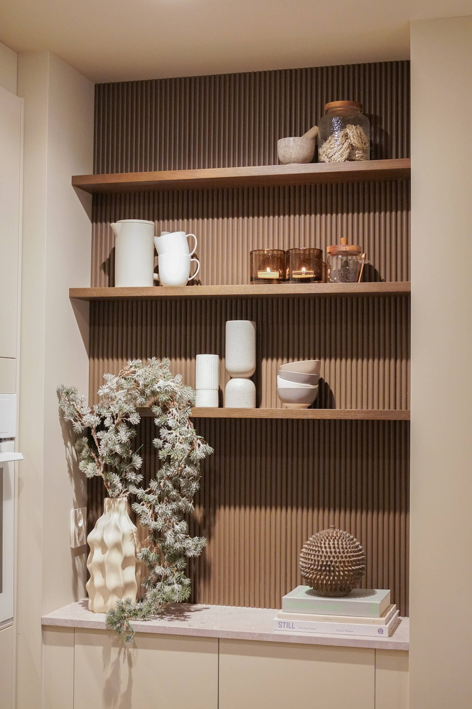 Veggen i kaffenisjen, der hyllene er festet er dekket med rillede dekorplater fra Deco Systems, malt i en egenkomponert farge som ligner beisfargen på kjøkkenøya