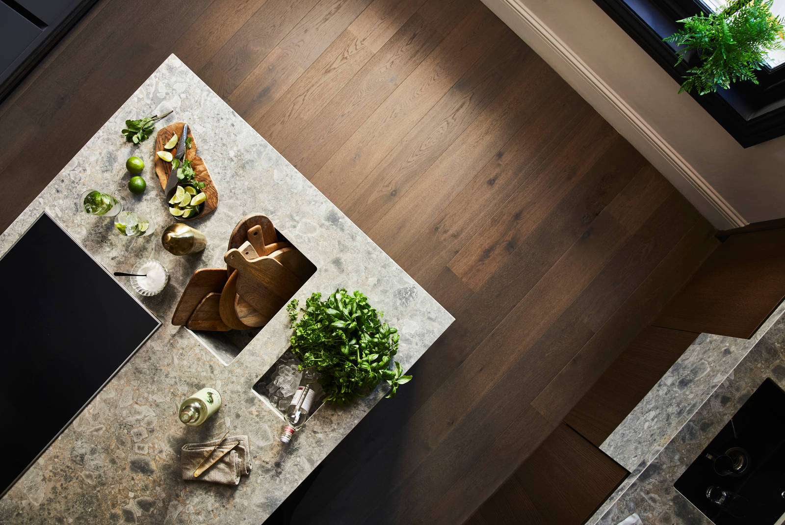 Birds eye view of kitchen island with Dekton in Ceppo worktop,wooden cutting boards with cut up lime fruits and a large plant of basil.