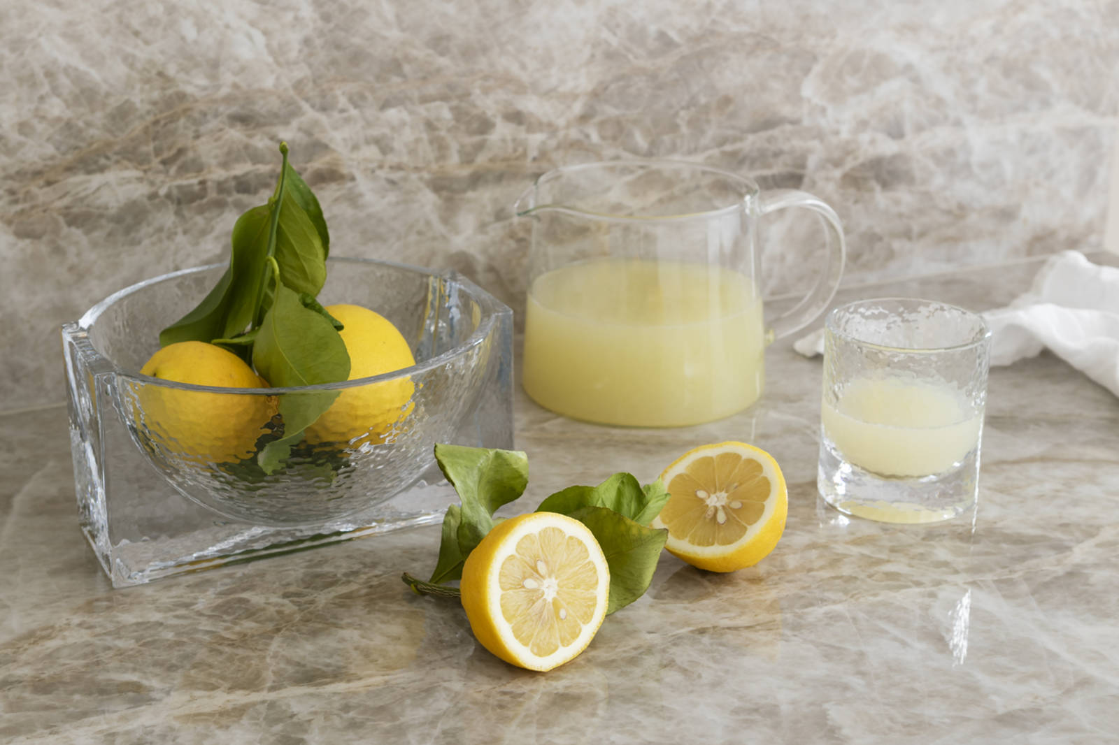 En glasskål med citroner, en kanna och ett dricksglas med citronsaft