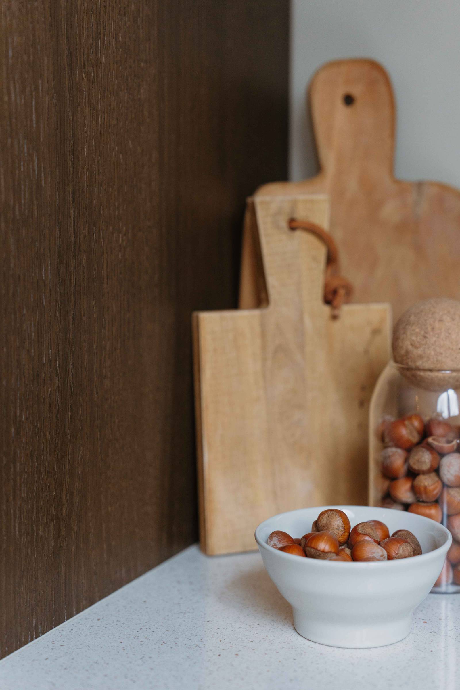 Skärbrädor och en keramisk skål på köksbänken i Liv och Hallvards Signatur Ekbacken-kök från Marbodal, med brunbetsad fanerad eklucka och bänkskiva i kvartskomposit