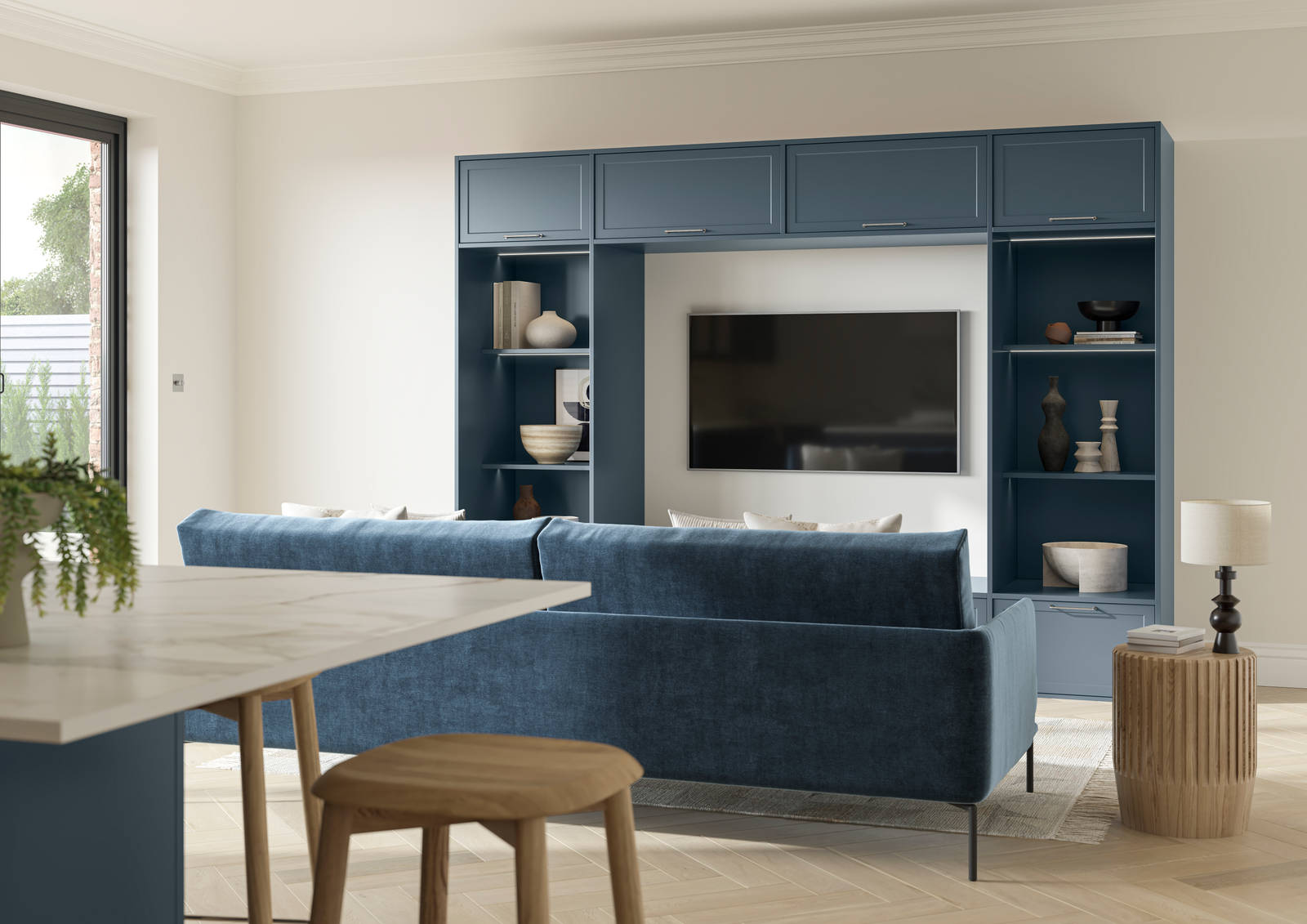 Cabinets and open shelves around a wall mounted TV in the modern Shaker range Brunswick Voyage Blue, matching blue counch and kitchen island in the foreground.