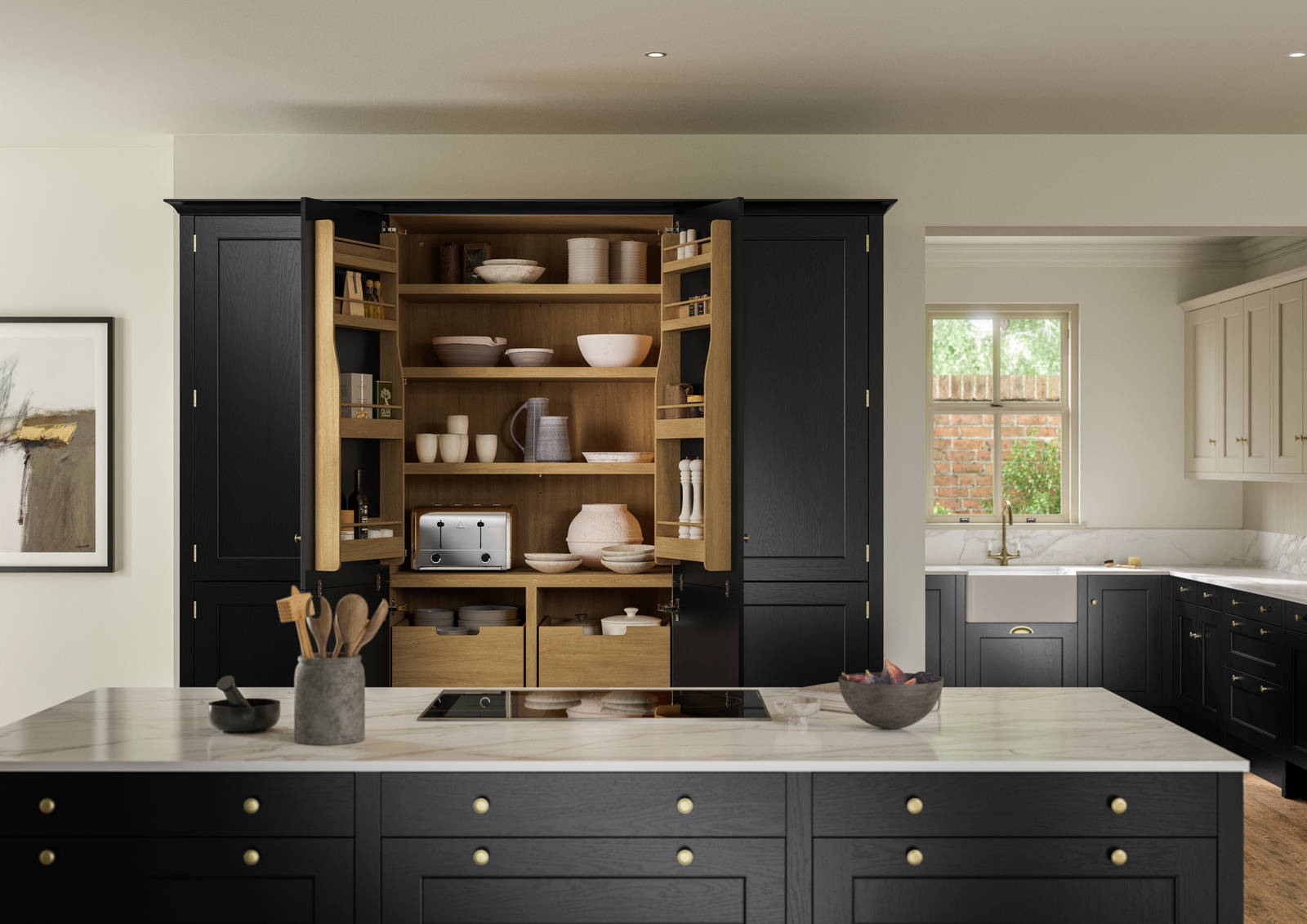 View over kitchen island in Traditional Shaker-style tactile woodgrain Ludlow Sumi Black kitchen, opened tall oak larder cabinets, brass accessories, marbled white and grey worktop, white ceramic sink and brass tap.