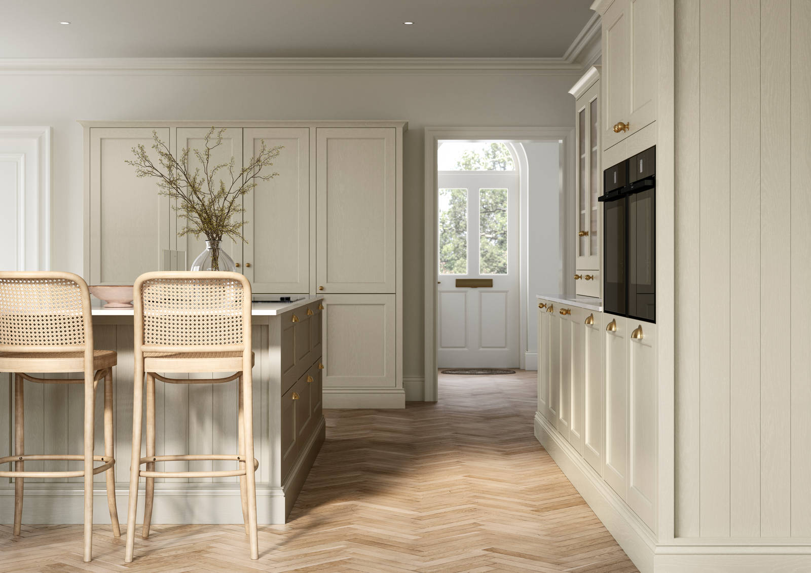 Traditional Shaker-style kitchen Ludlow Parchment with tactile woodgrain, tall cabinets, brass cup handles and knobs, integrated ovens, a kitchen island with rattan bar stools, a vase holding foliage, and light wood herringbone flooring.