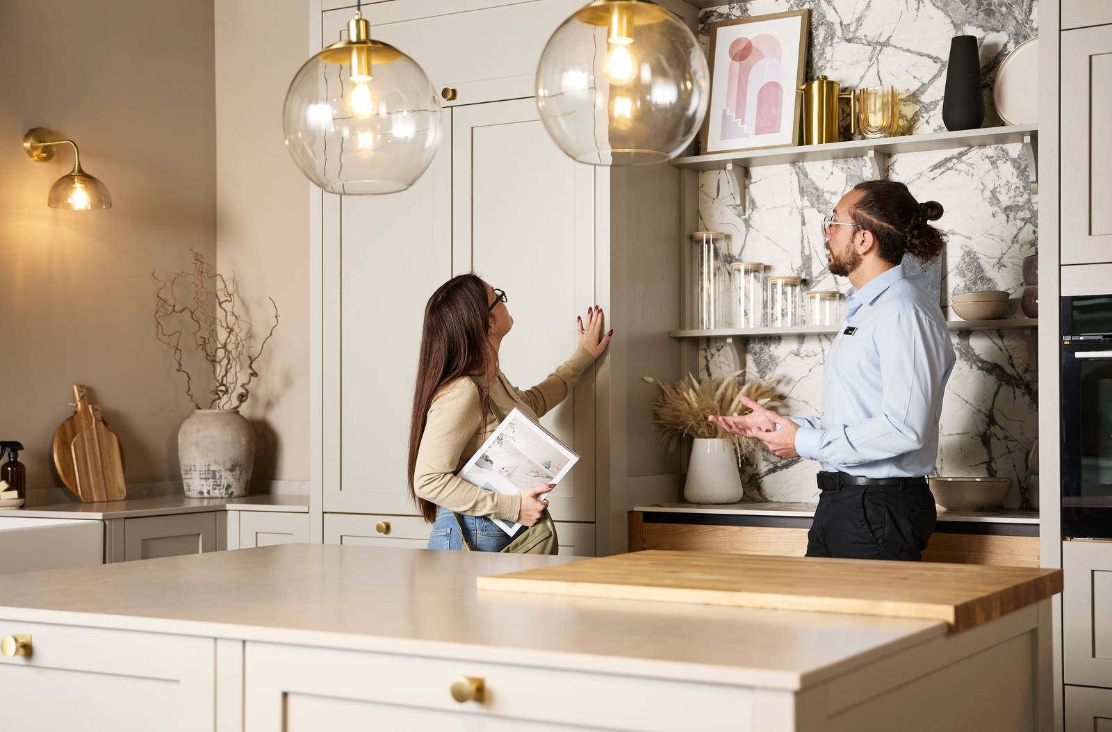 Woman holding a brochure and feeling a Shaker front with her hand while speaking to a kitchen designer in a Magnet Showroom.
