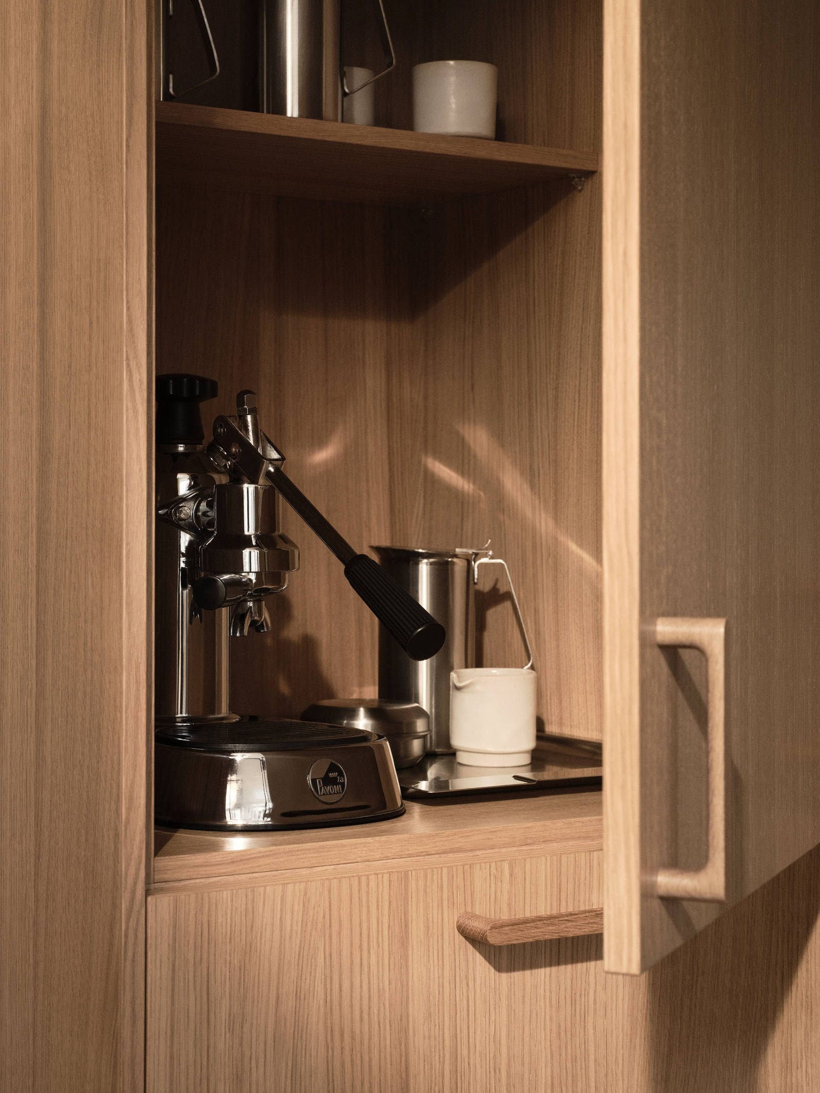 Öppnat skåp i Siri Barjes kök, ekskåp med kaffemaskin i skåpet, handtag i ek.